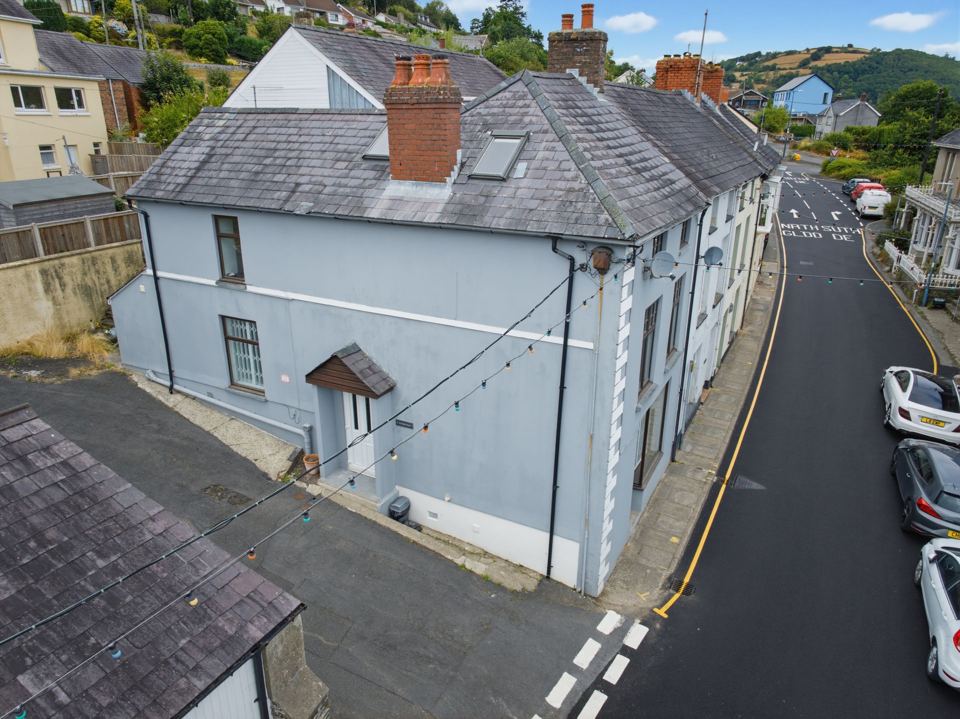 Aerial view of a pale blue corner building on a narrow street with parked cars and neighboring houses.