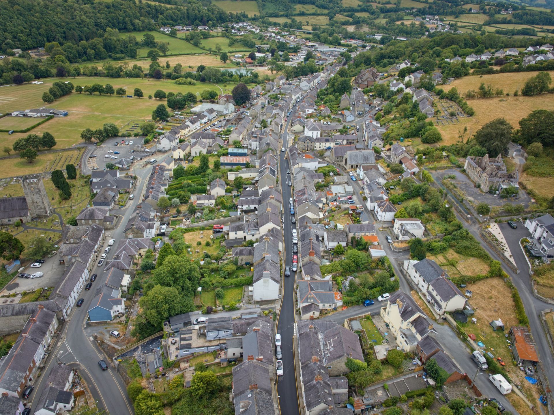 Aerial view of a small town street lined with houses, trees, and fields in a green valley.