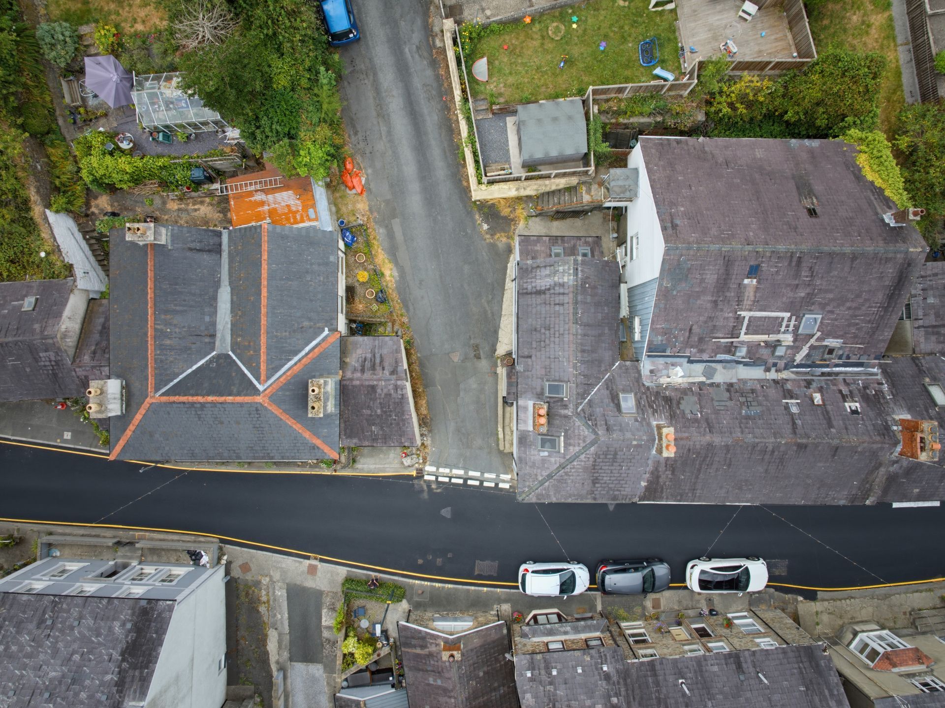 Aerial view of houses and parked cars along a wet residential street.