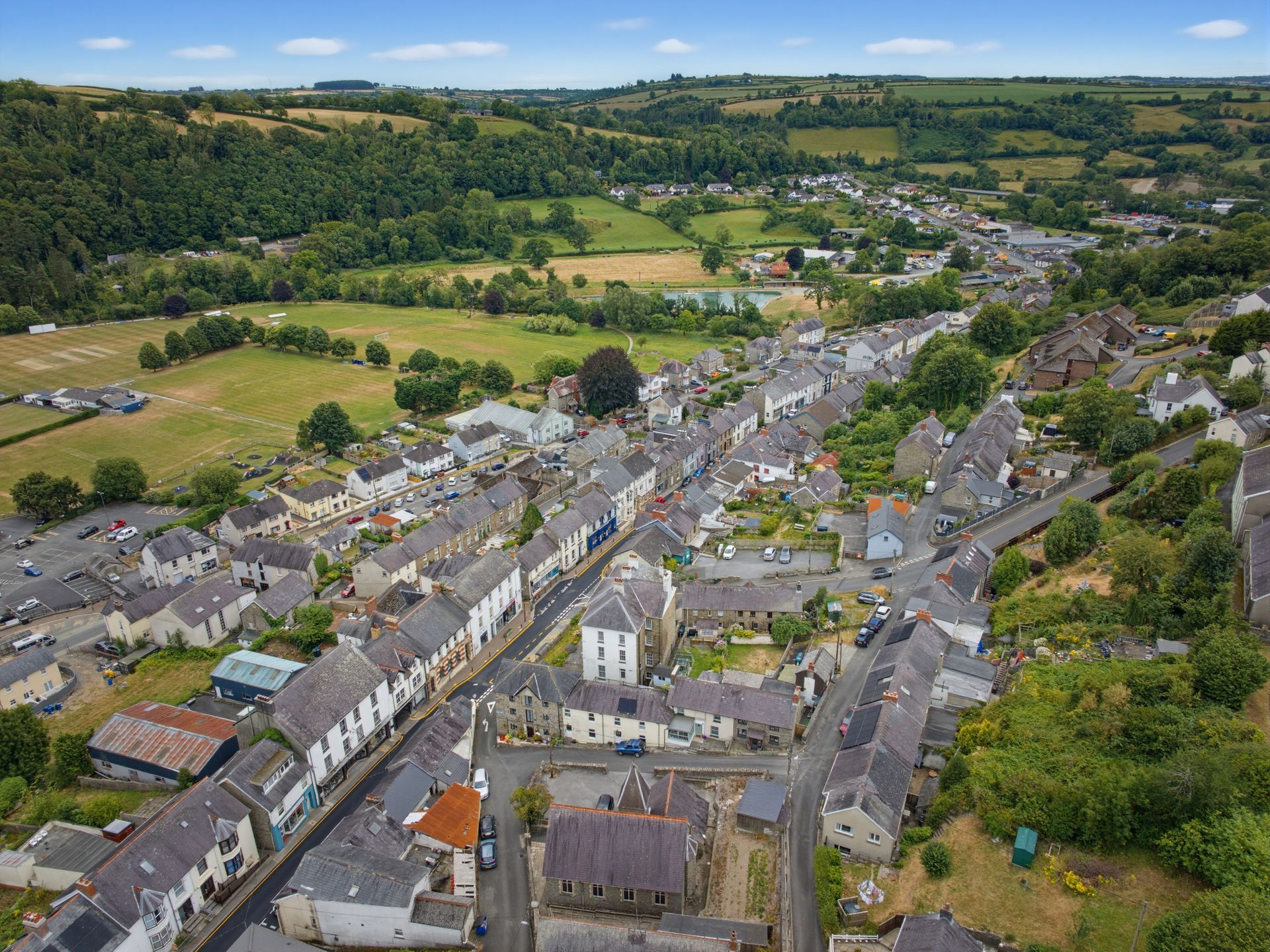 Aerial view of a small village with gray rooftops, winding roads, and green fields and hills beyond.