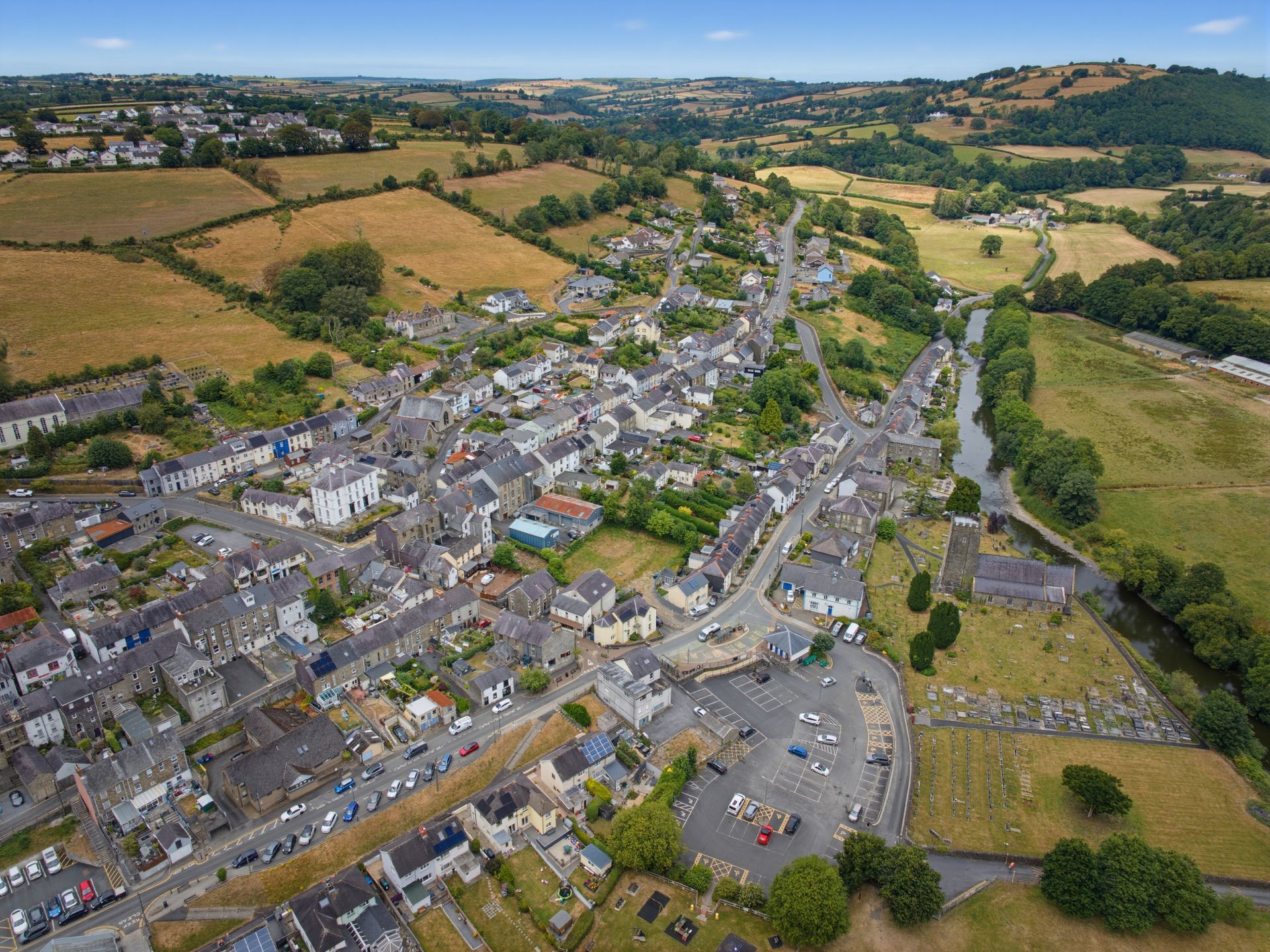 Aerial view of a small village with gray-roofed houses, roads, and surrounding खेतs and green hills