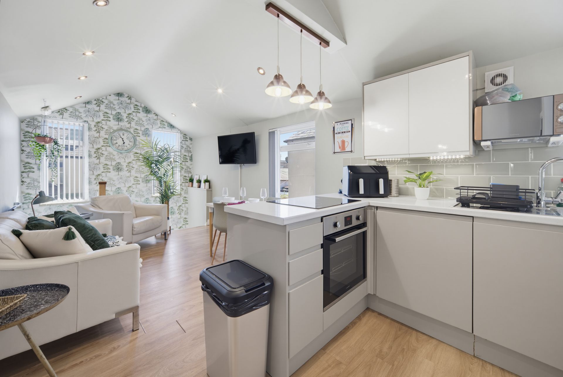 Bright open-plan kitchen and living room with white cabinets, gray sofa, and vaulted ceiling