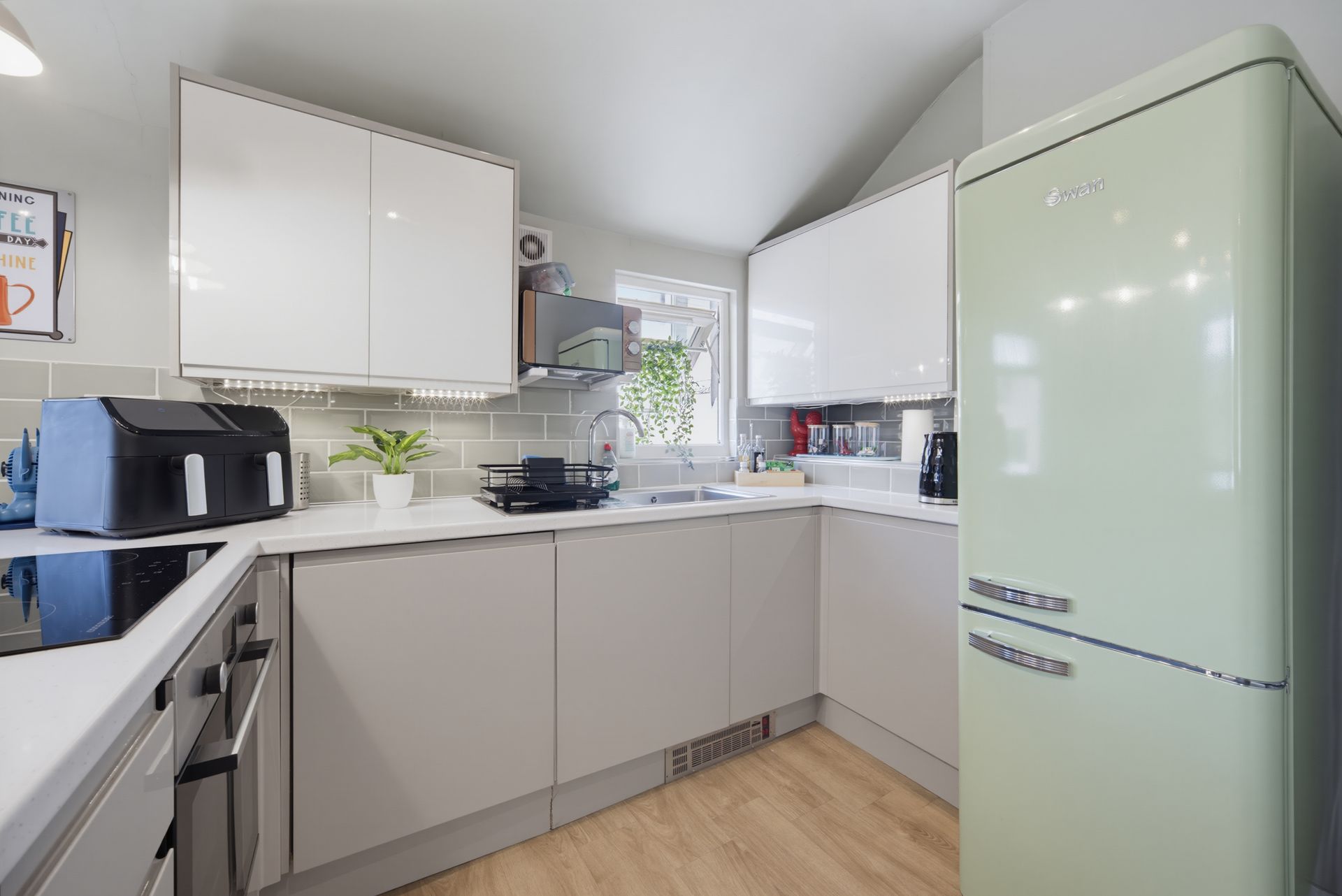 Bright modern kitchen with white cabinets, pale green fridge, and light wood floor