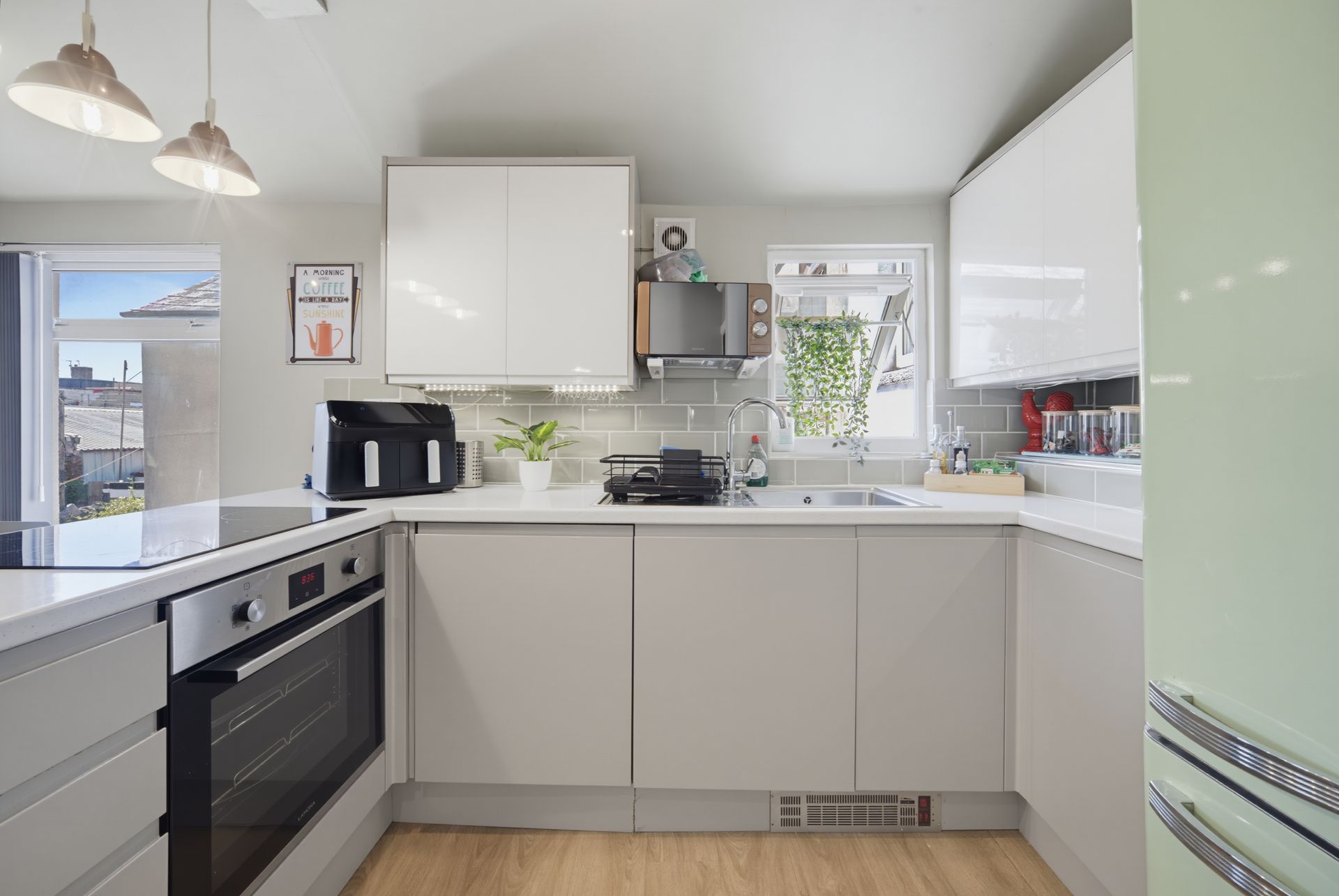 Modern white kitchen with stainless appliances, light wood floor, and large windows looking outside
