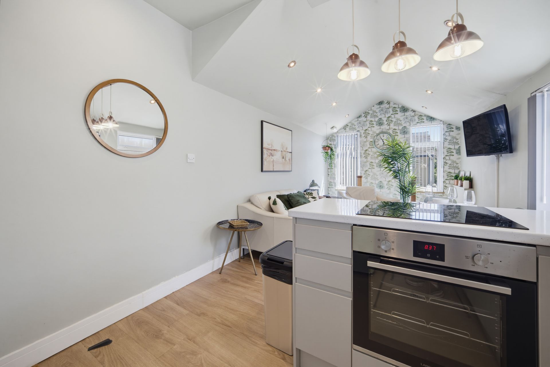 Bright modern kitchen with island, pendant lights, round mirror, and a window bench under vaulted ceiling