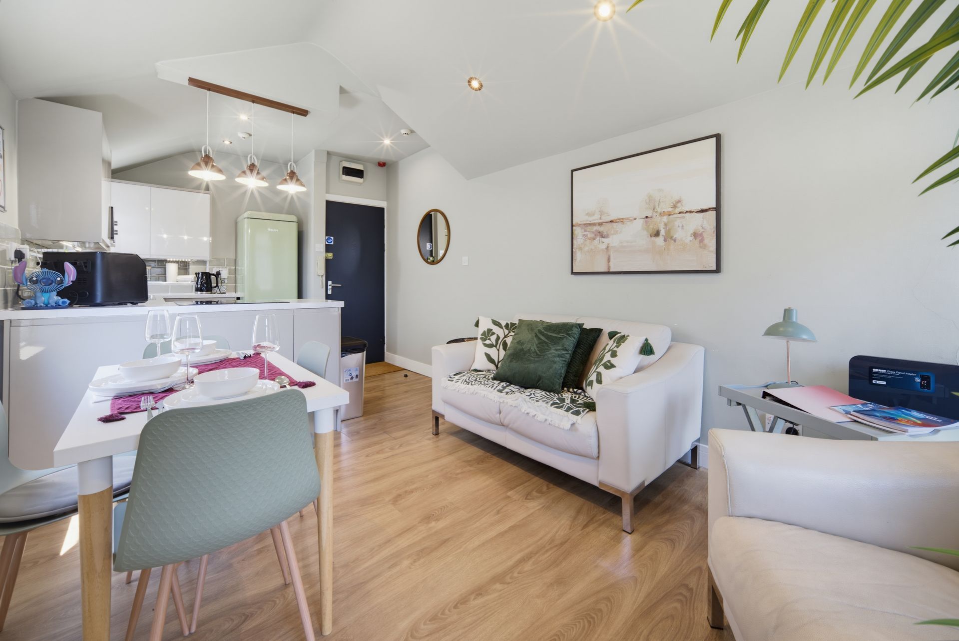 Bright modern living-dining room with white sofa, dining table, wood floors, and open kitchen.