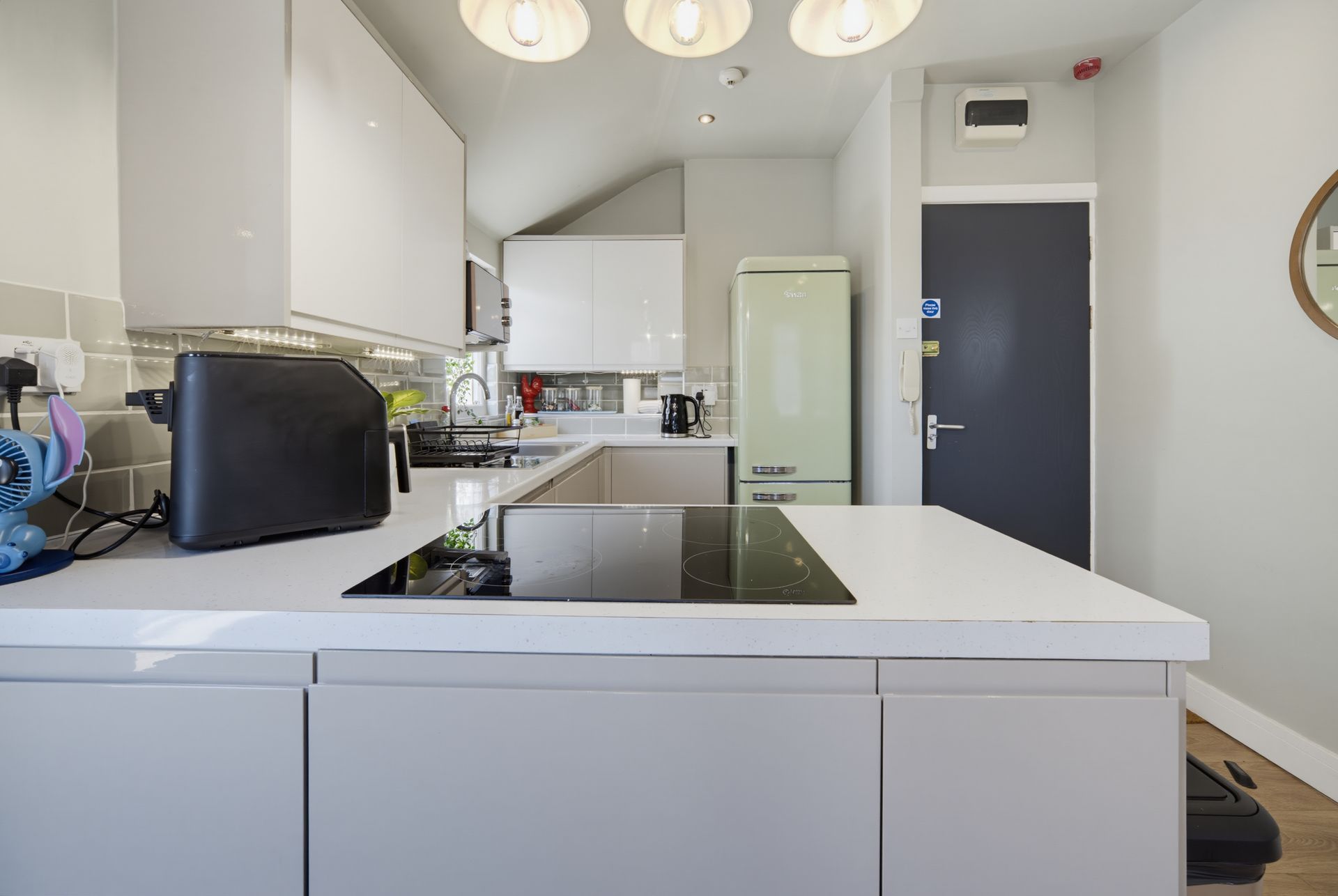 Modern white kitchen with island, stovetop, sink, and black toaster under ceiling lights