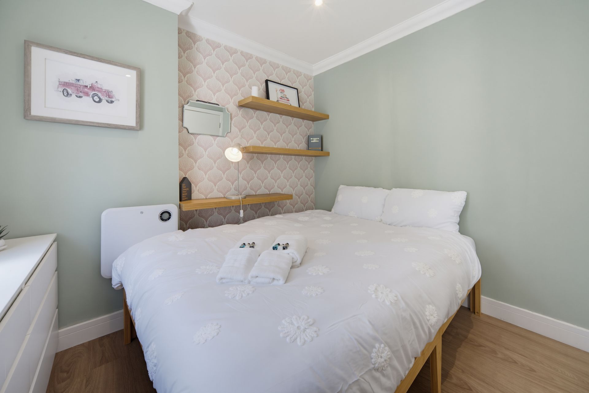 Bright bedroom with white bed, mint green walls, wooden shelves, and framed wall art.