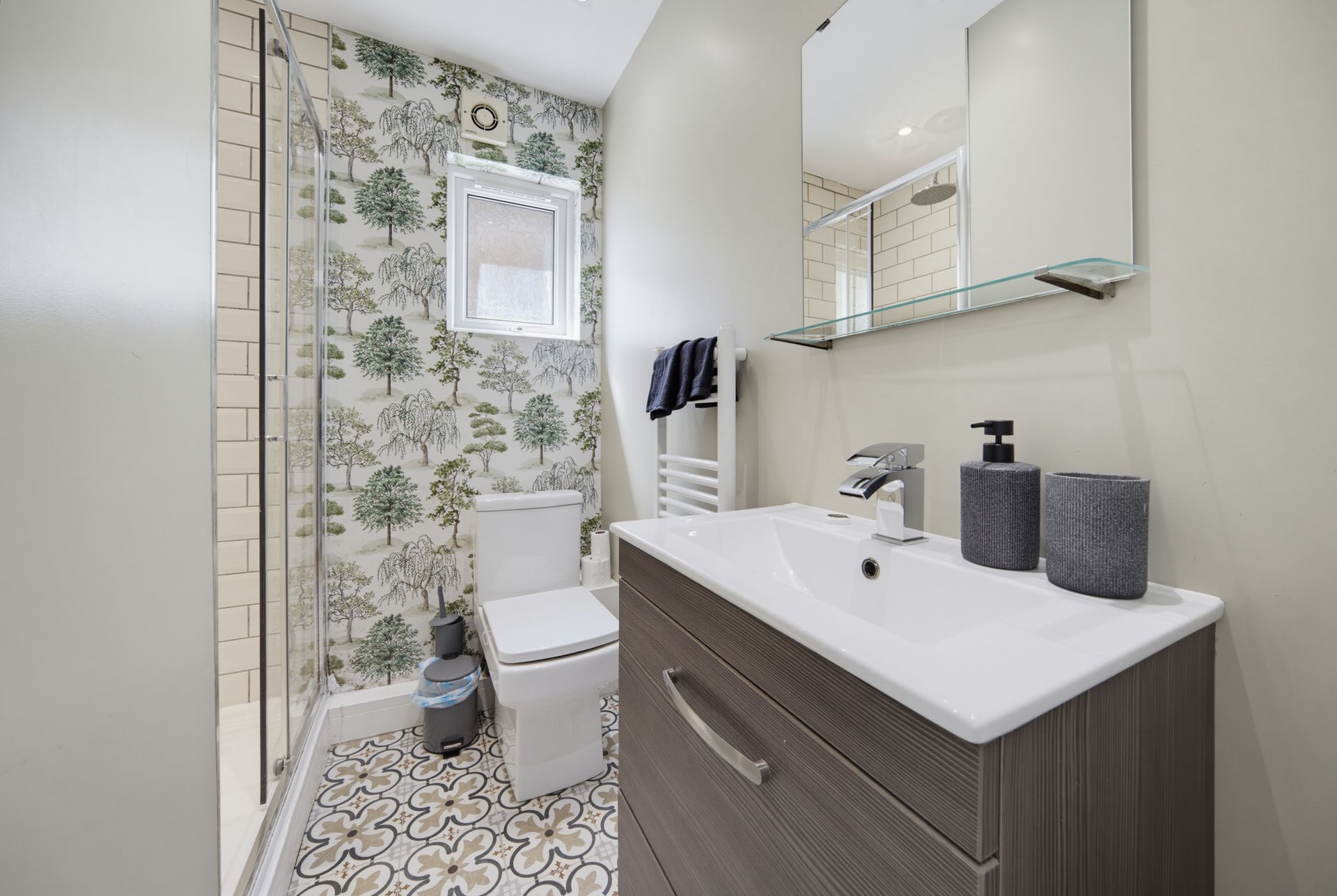 Compact bathroom with patterned wallpaper, white toilet, and dark wood vanity with sink and mirror.