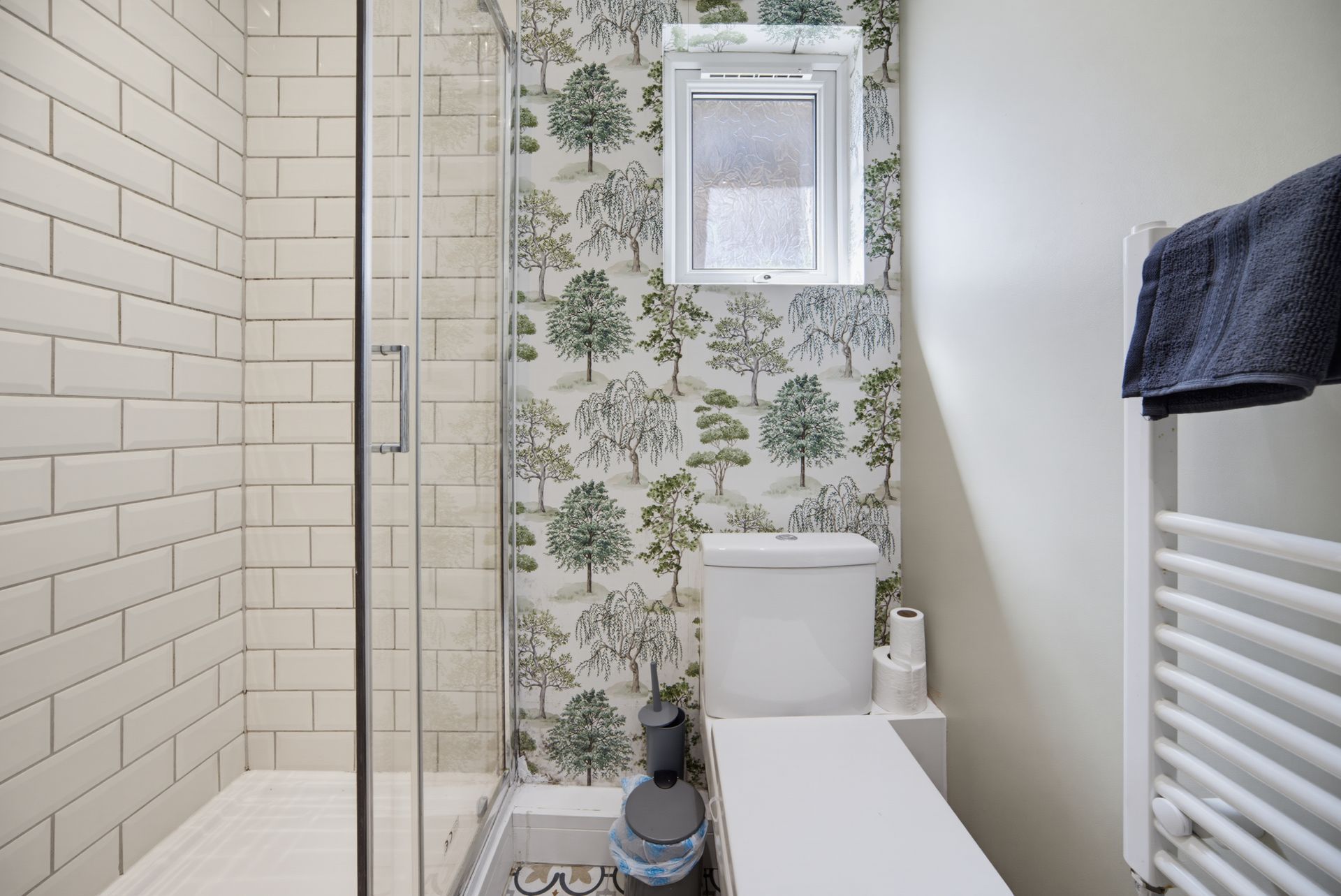 Small bathroom with shower, white toilet, floral wallpaper, and towel radiator.