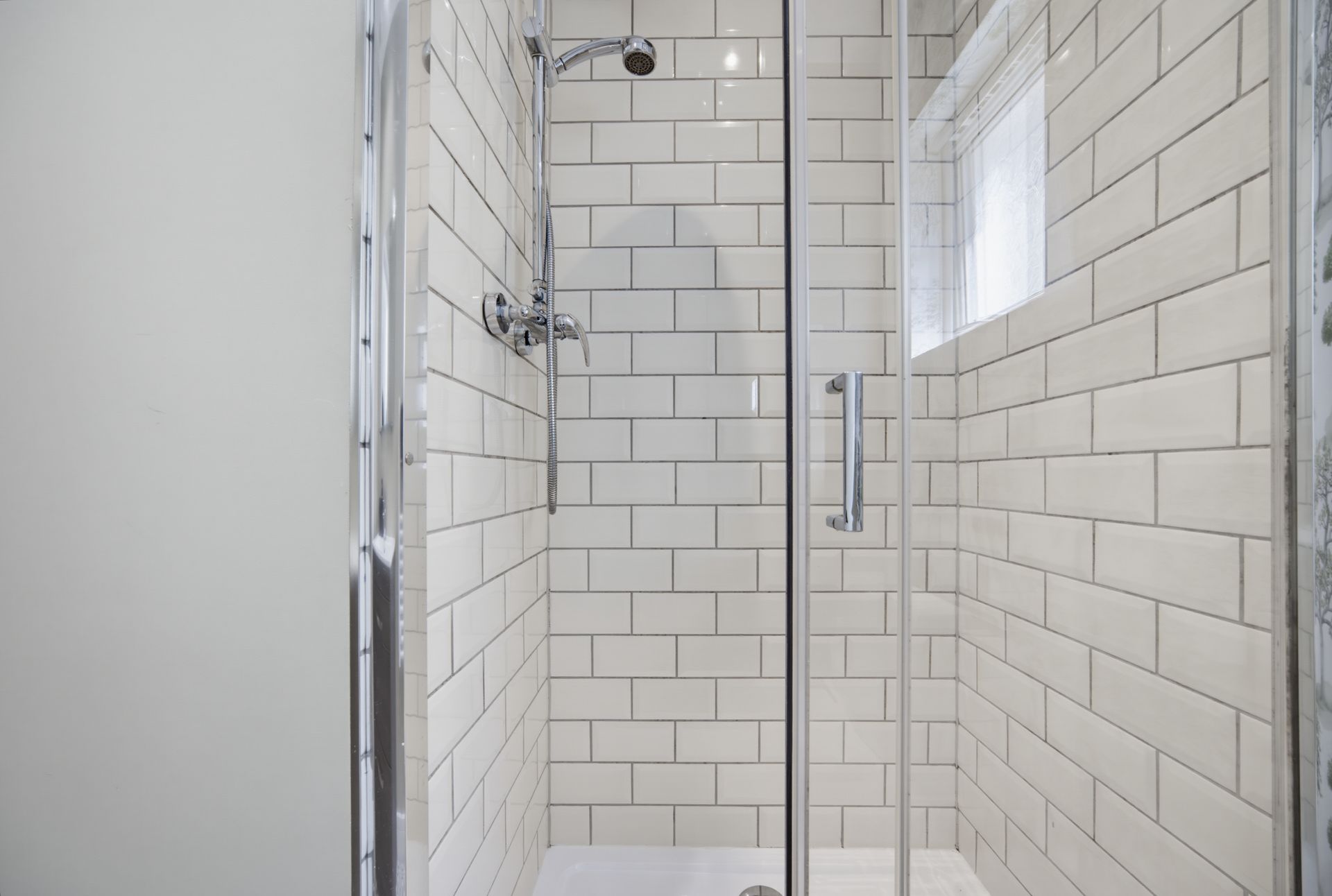 Small tiled walk-in shower with glass door, chrome fixtures, and white subway tiles