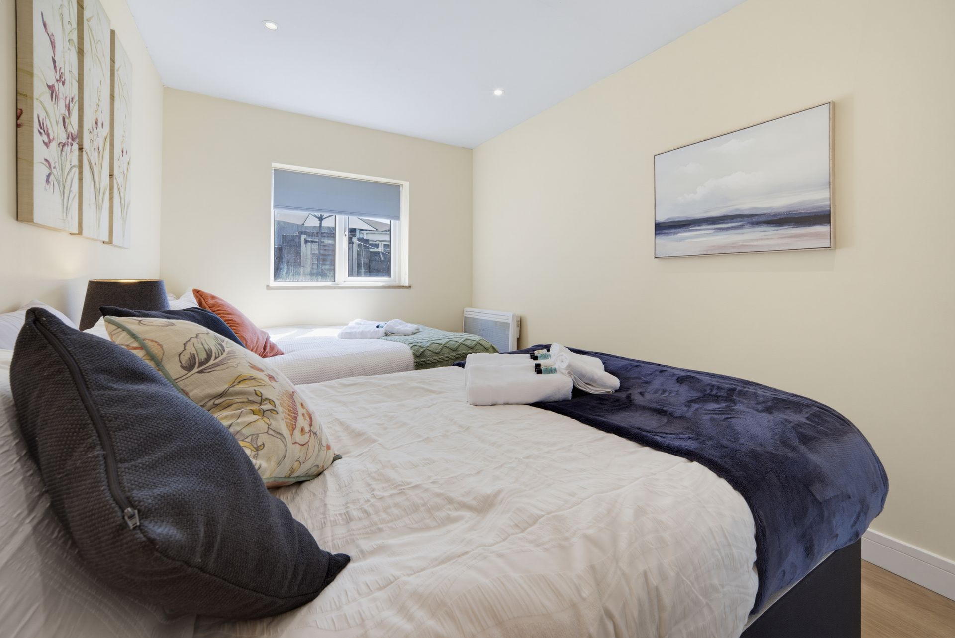 Bright bedroom with two beds, white bedding, dark throws, wall art, and a small window