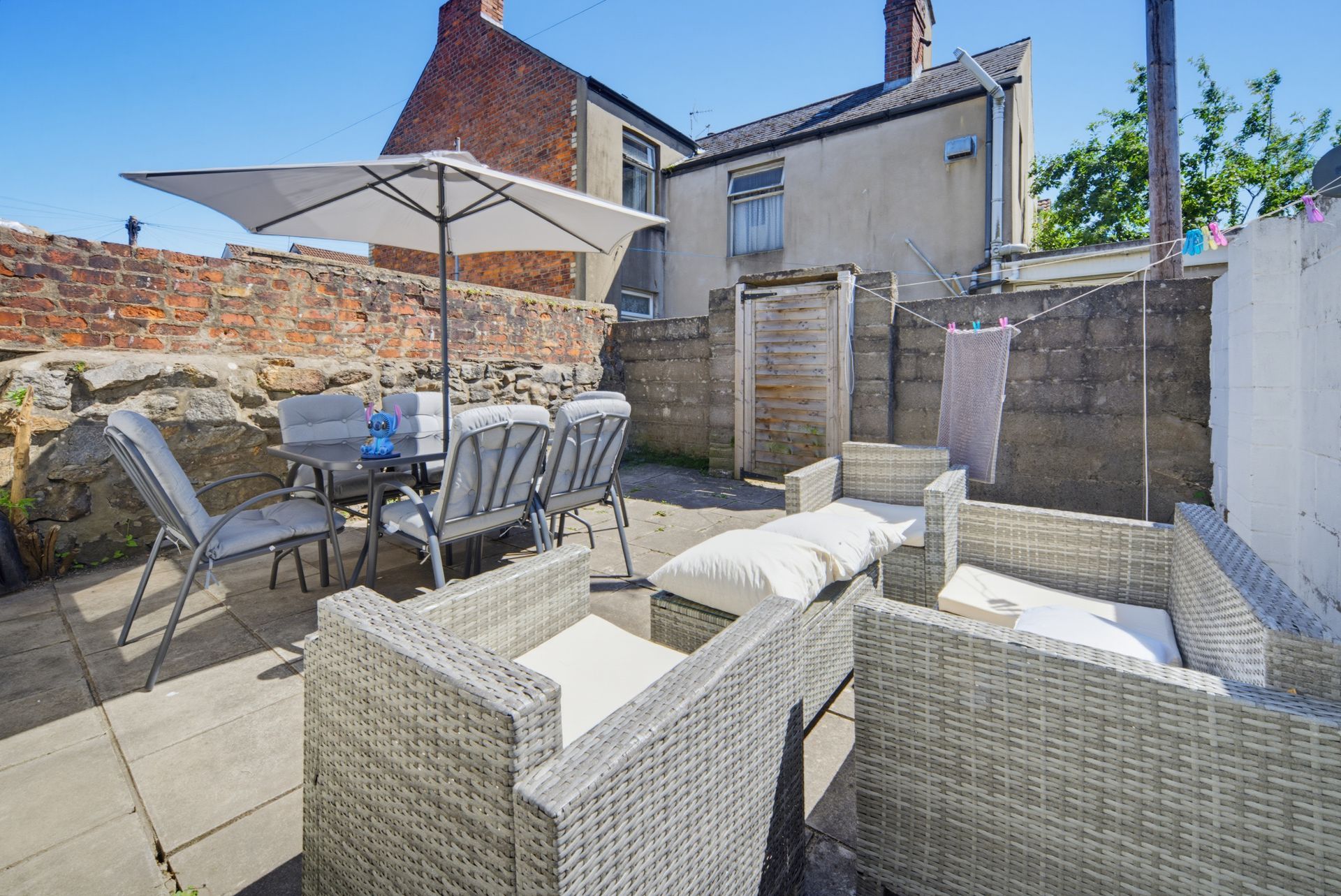 Patio with wicker seating, dining table and umbrella in a sunny walled courtyard