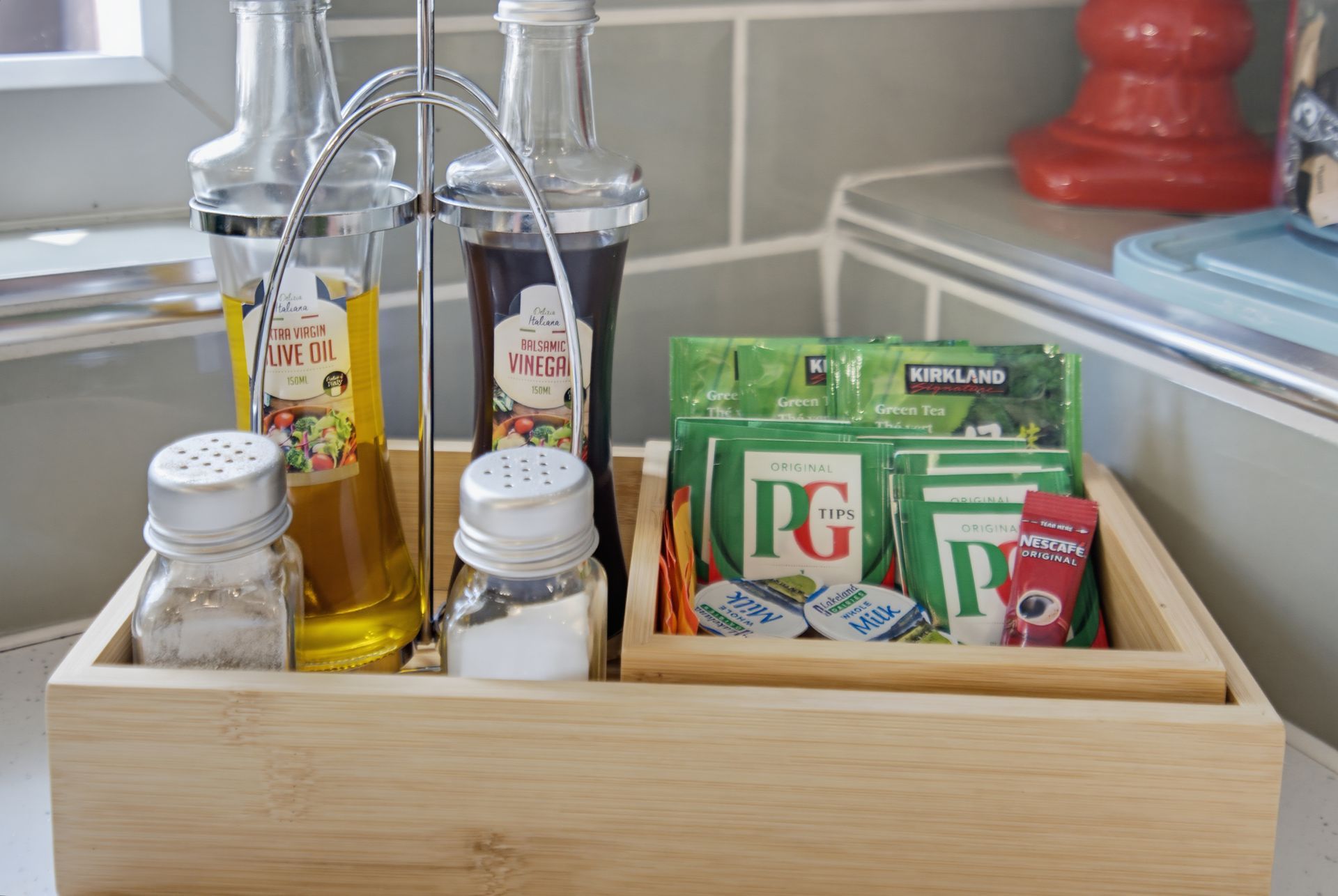 Wooden tray with tea packets, sugar jars, and bottles of oil on a kitchen counter.