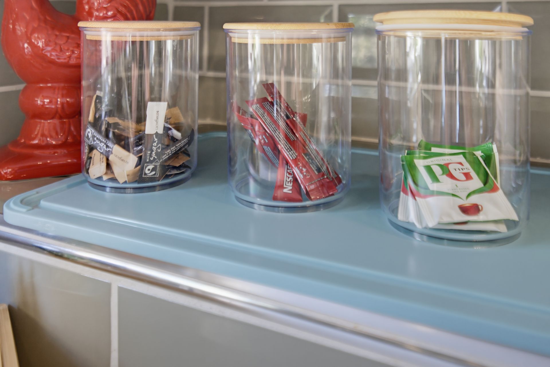 Three clear jars with snack wrappers on a blue countertop beside a red object.