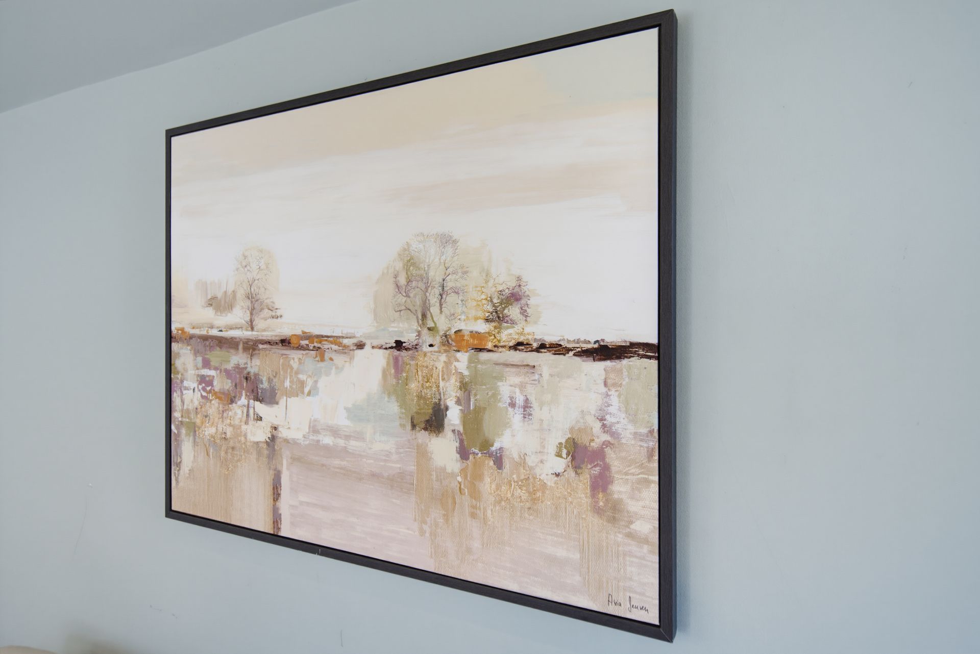 Abstract landscape painting in soft beige tones with black frame on a light blue wall
