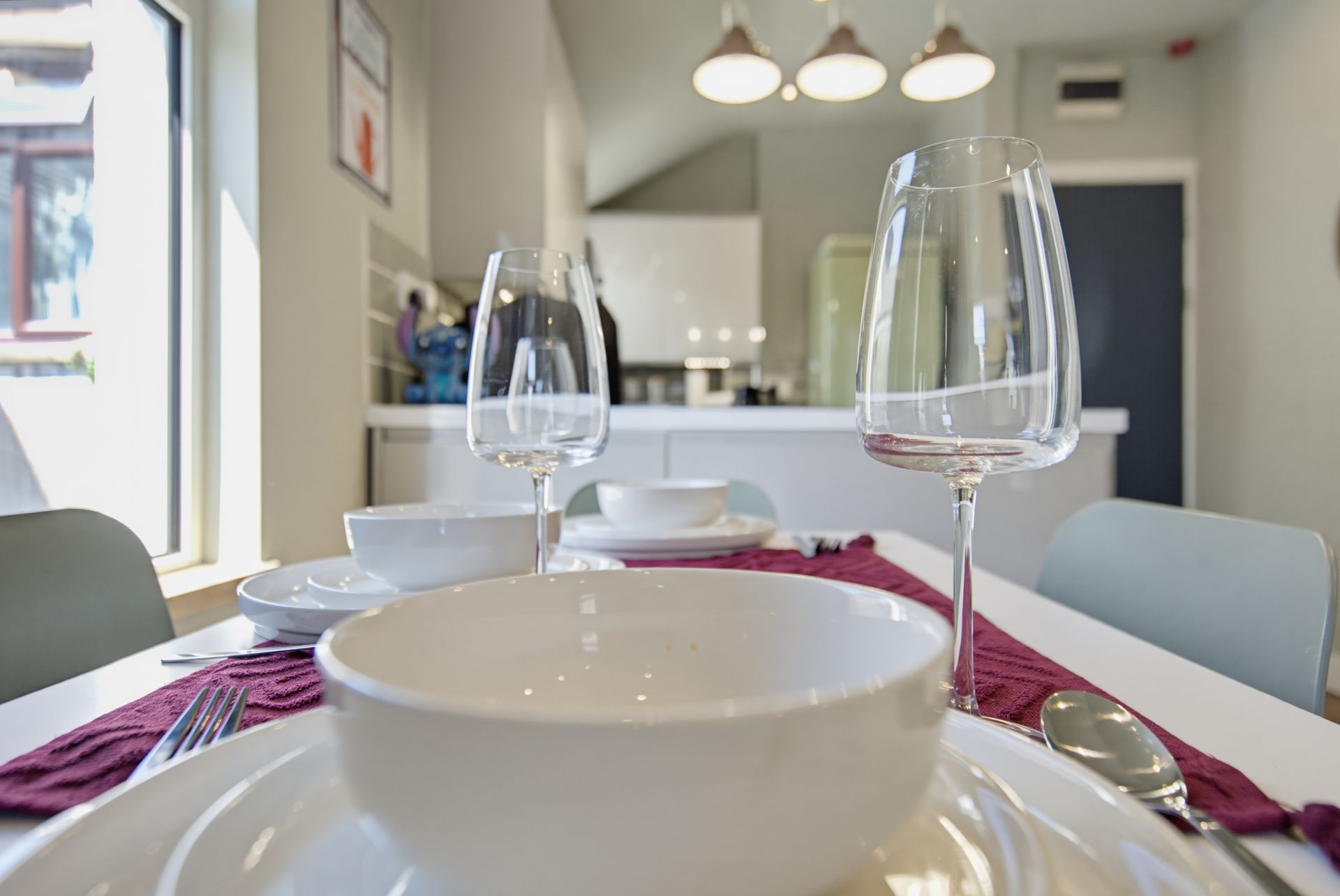 Set dining table with white bowls, wine glasses, and red napkin in a bright kitchen-dining room