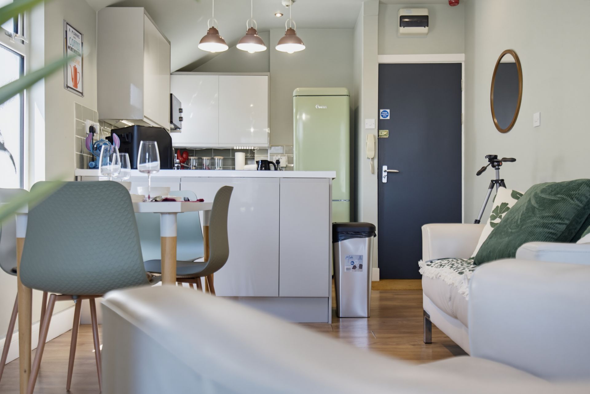 Bright modern kitchen and living room with white cabinets, gray chair, white sofa, and pendant lights