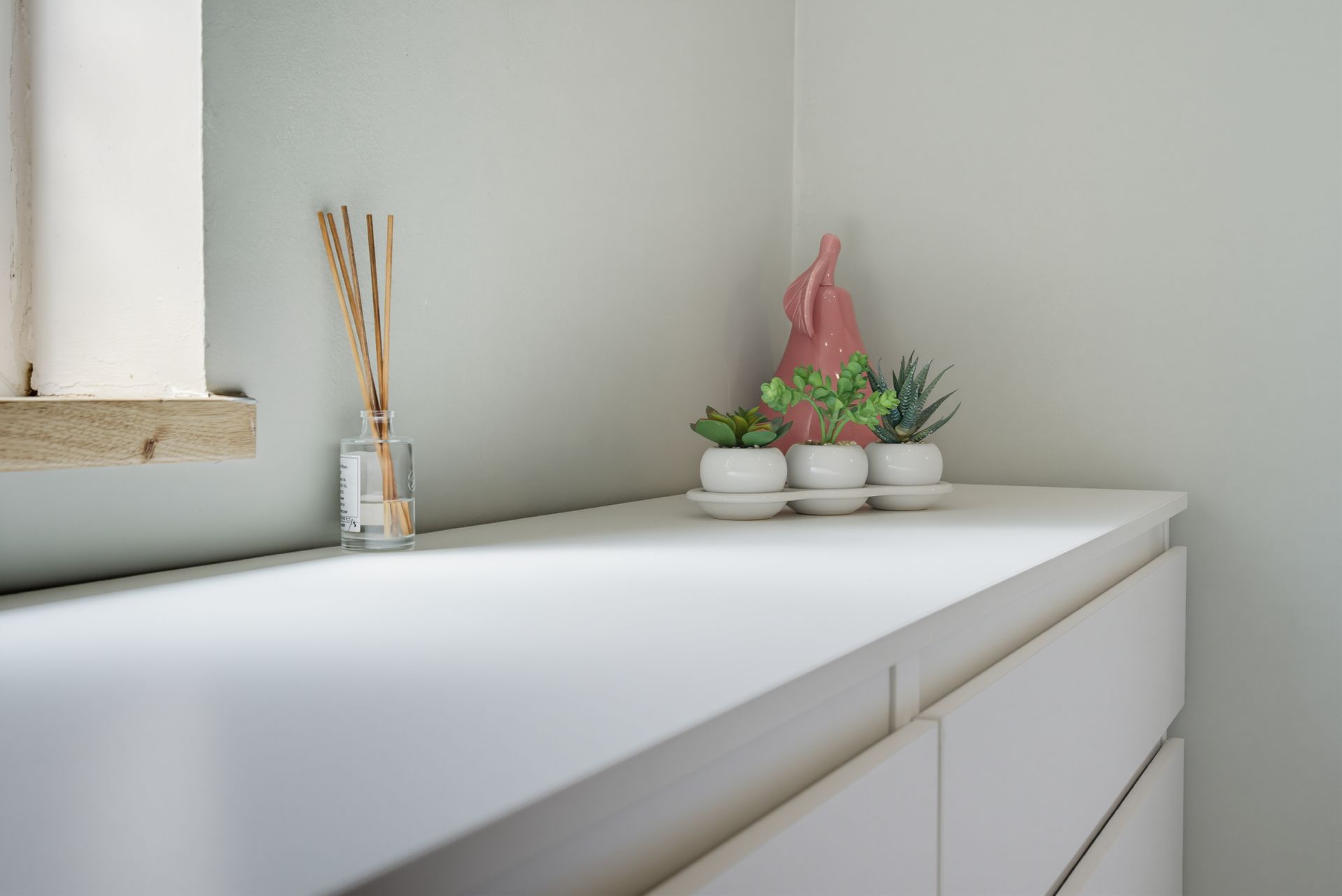 White dresser by a window with reed diffuser and small potted plants on top
