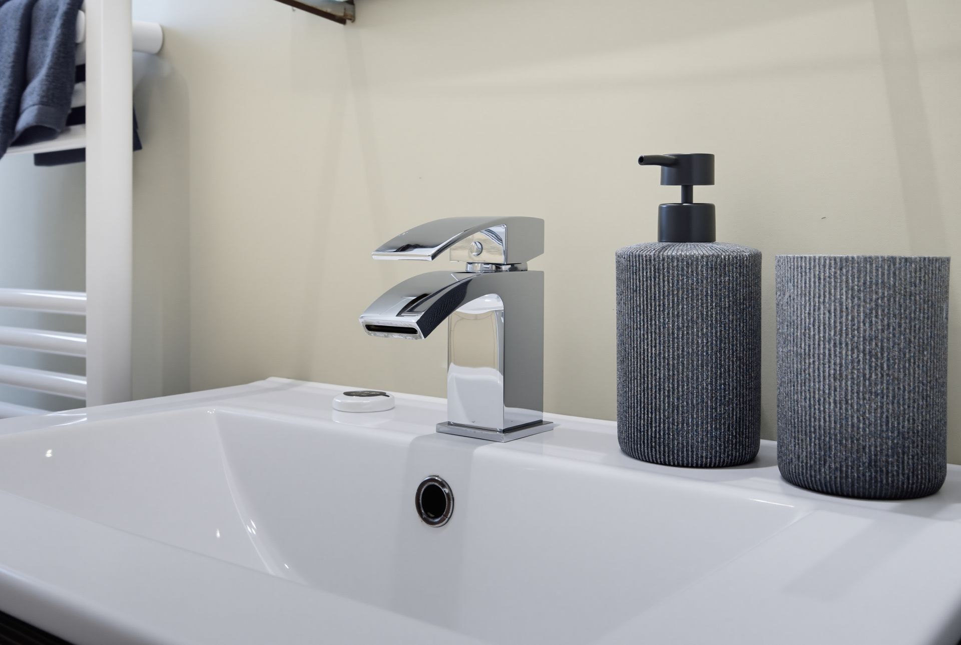 Modern bathroom sink with chrome faucet, soap dispenser, and two dark textured containers on the counter