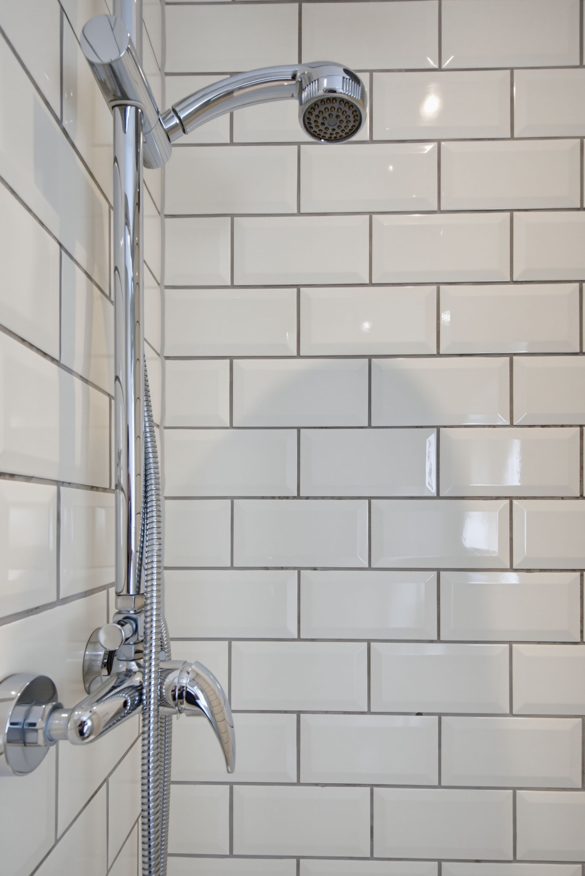 Chrome showerhead and controls against white subway tile in a bathroom.