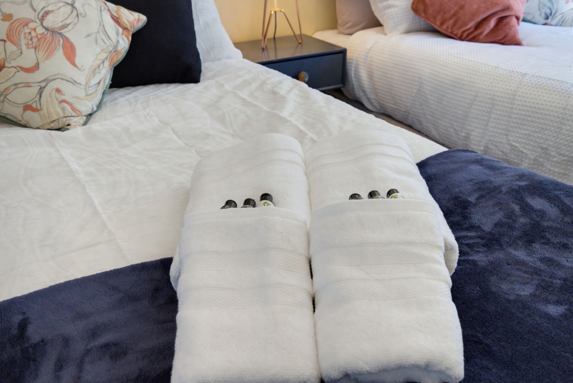 Two neatly folded white towels on a bed with dark blue blanket and patterned pillows