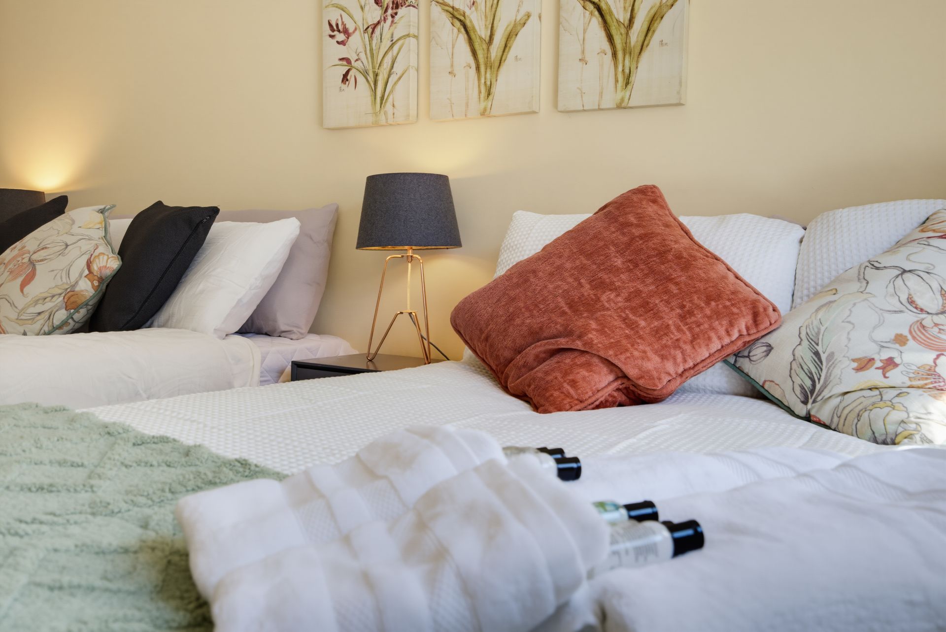 Cozy bedroom with two white beds, patterned pillows, a lamp, and wall art