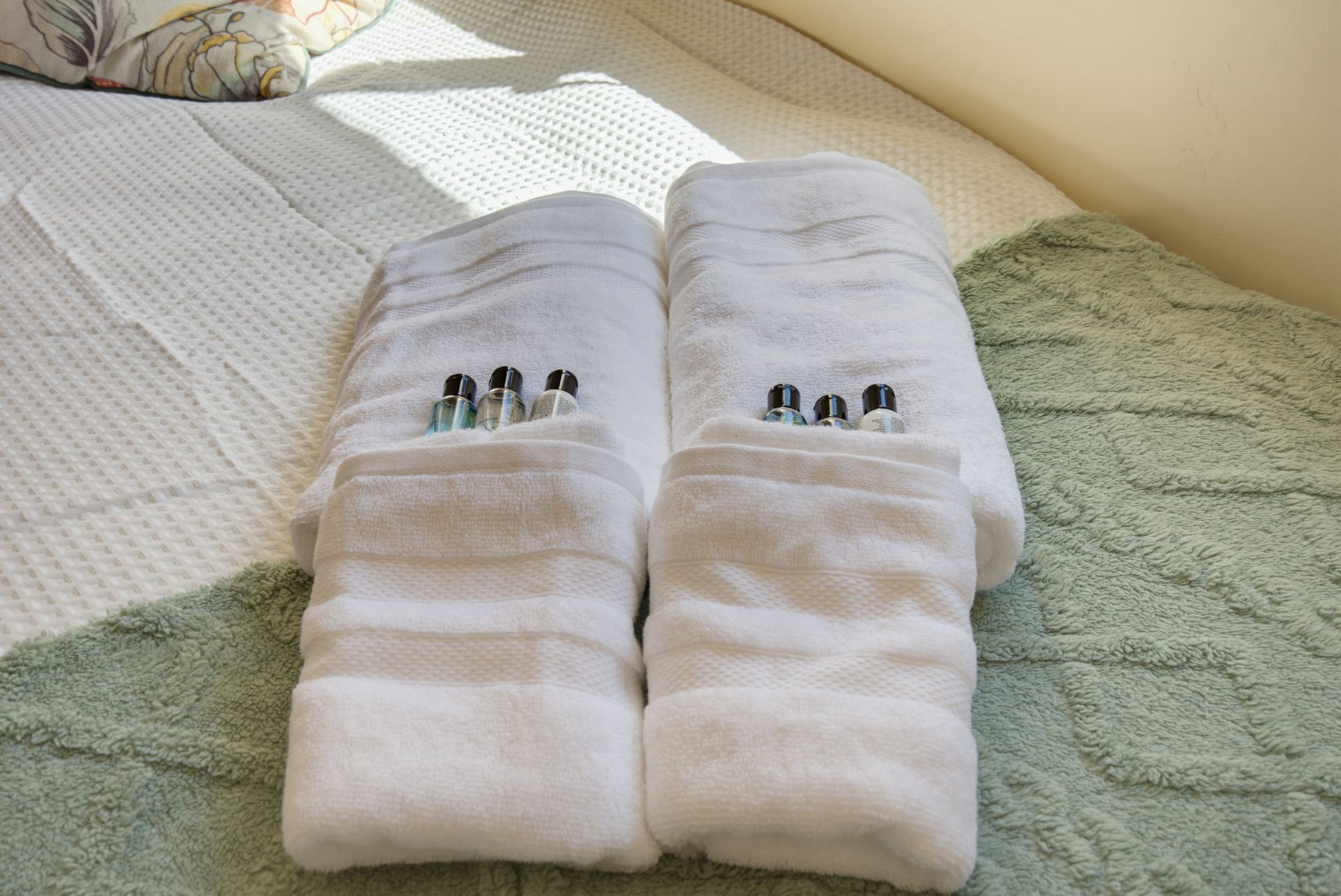 White folded towels with small toothbrushes arranged on a bed.