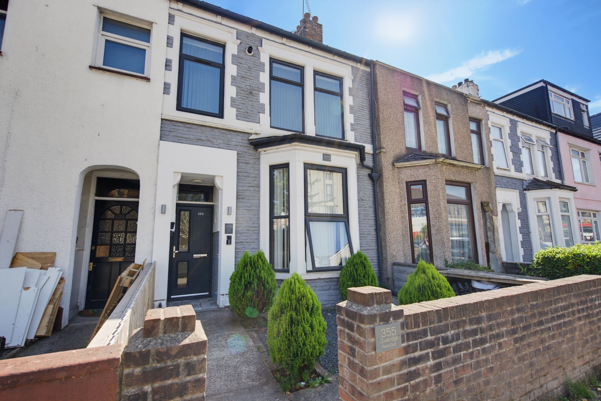 Row of terraced houses with a cream-fronted home and small front gardens on a sunny street