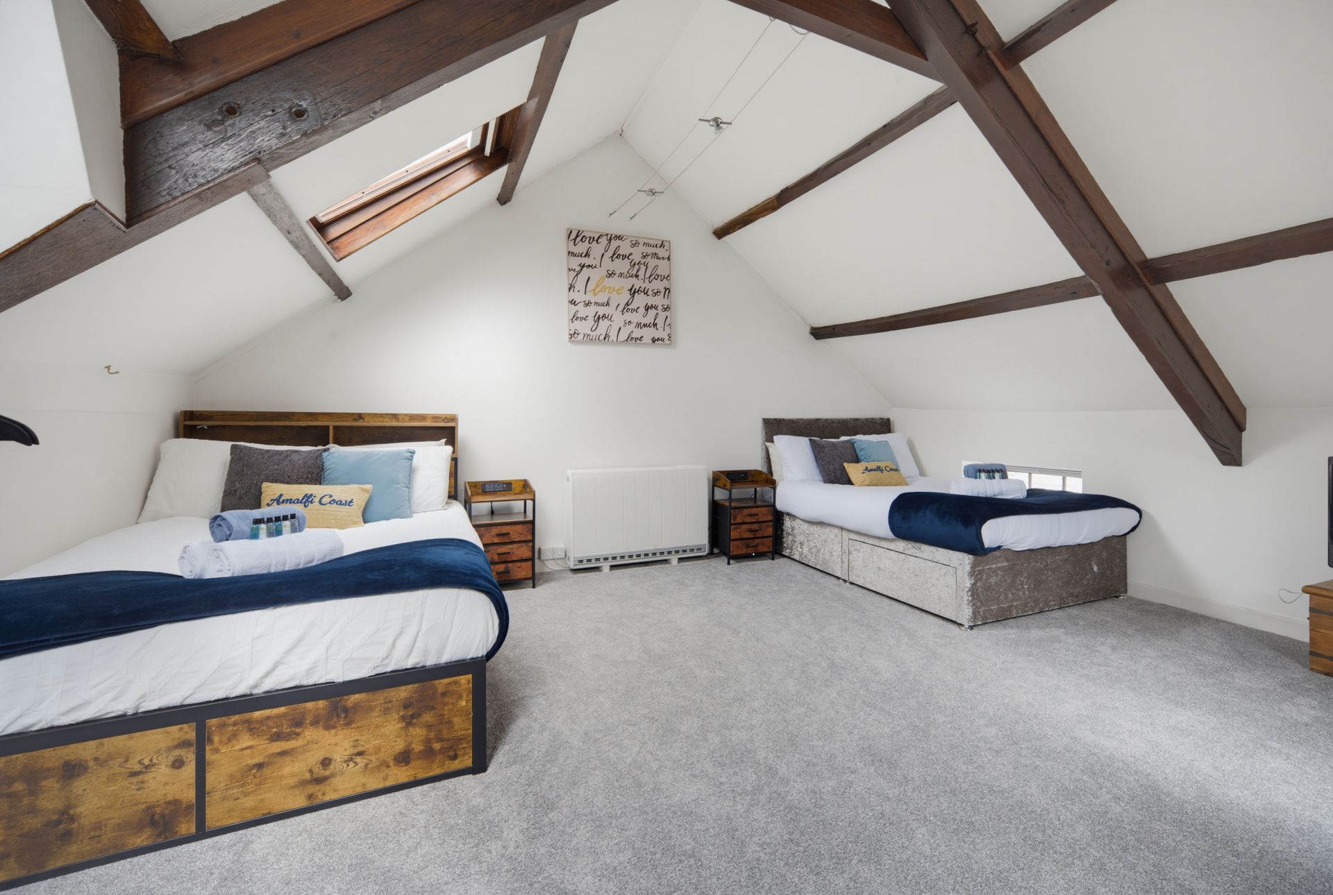 Spacious attic bedroom with two blue-and-white beds, sloped wooden beams, and light carpet.