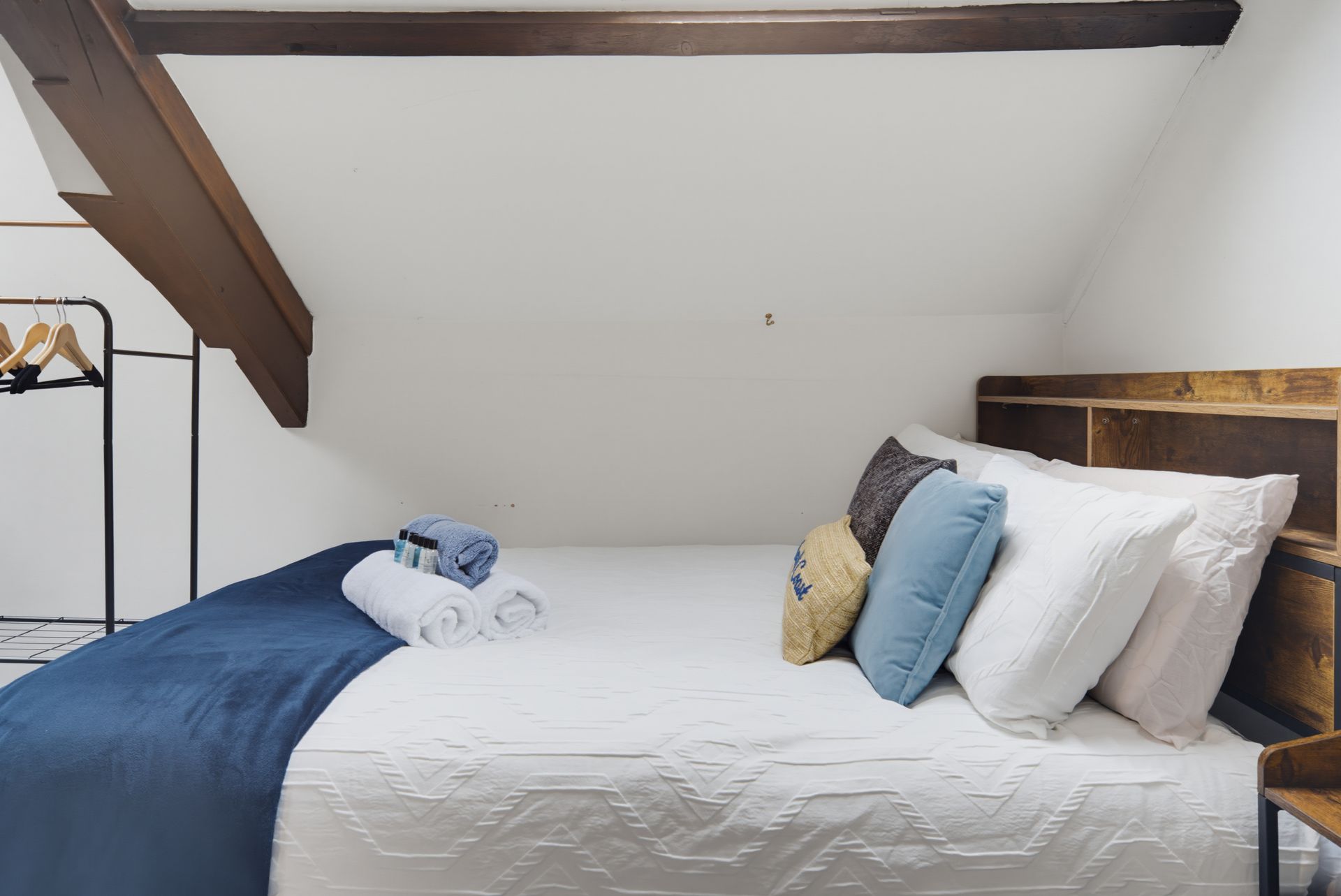 Cozy loft bedroom with white bed, blue blanket, pillows, and exposed wooden beams