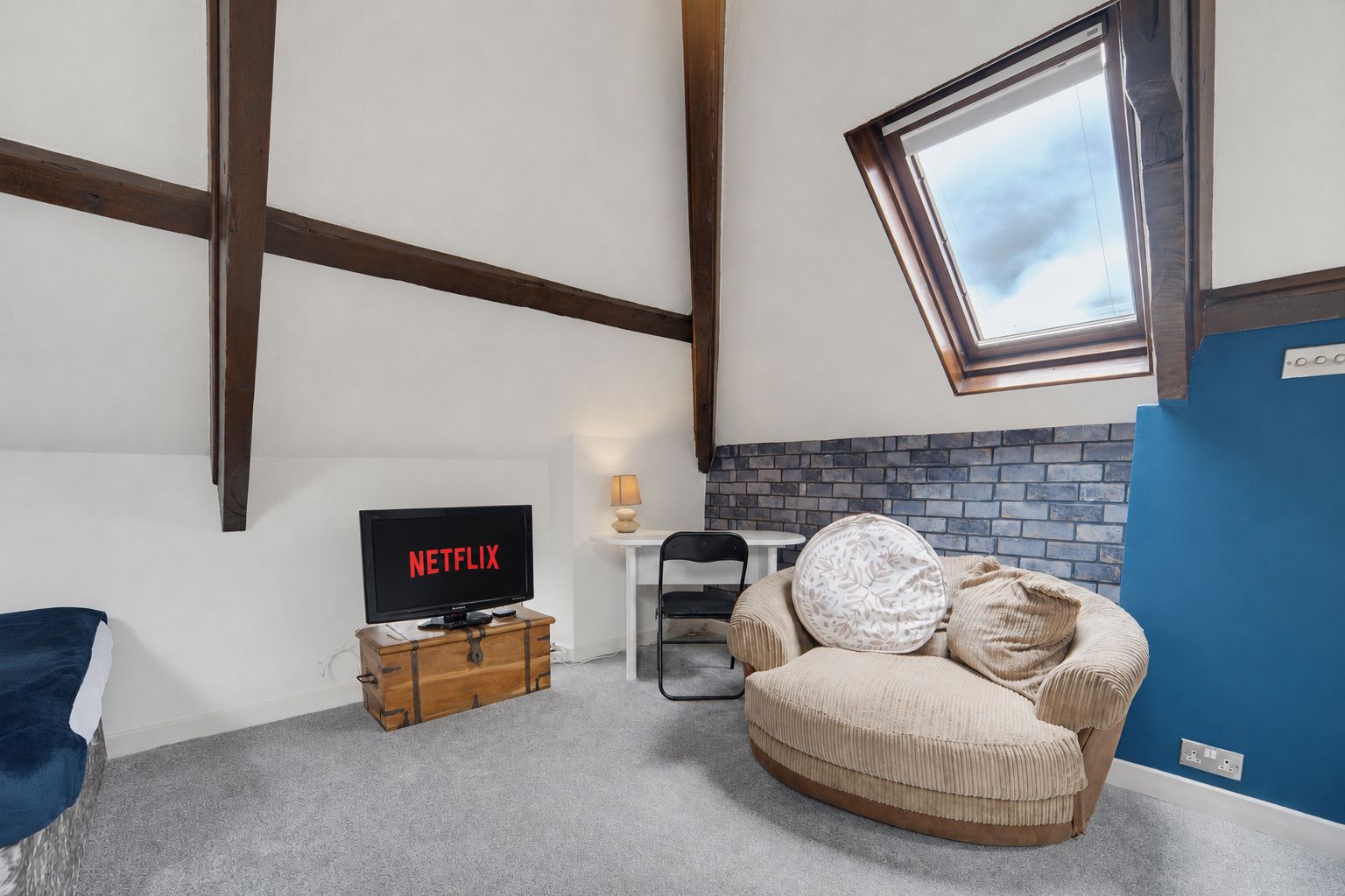 Cozy attic lounge with beige chair, TV on basket, skylight, and blue accent wall