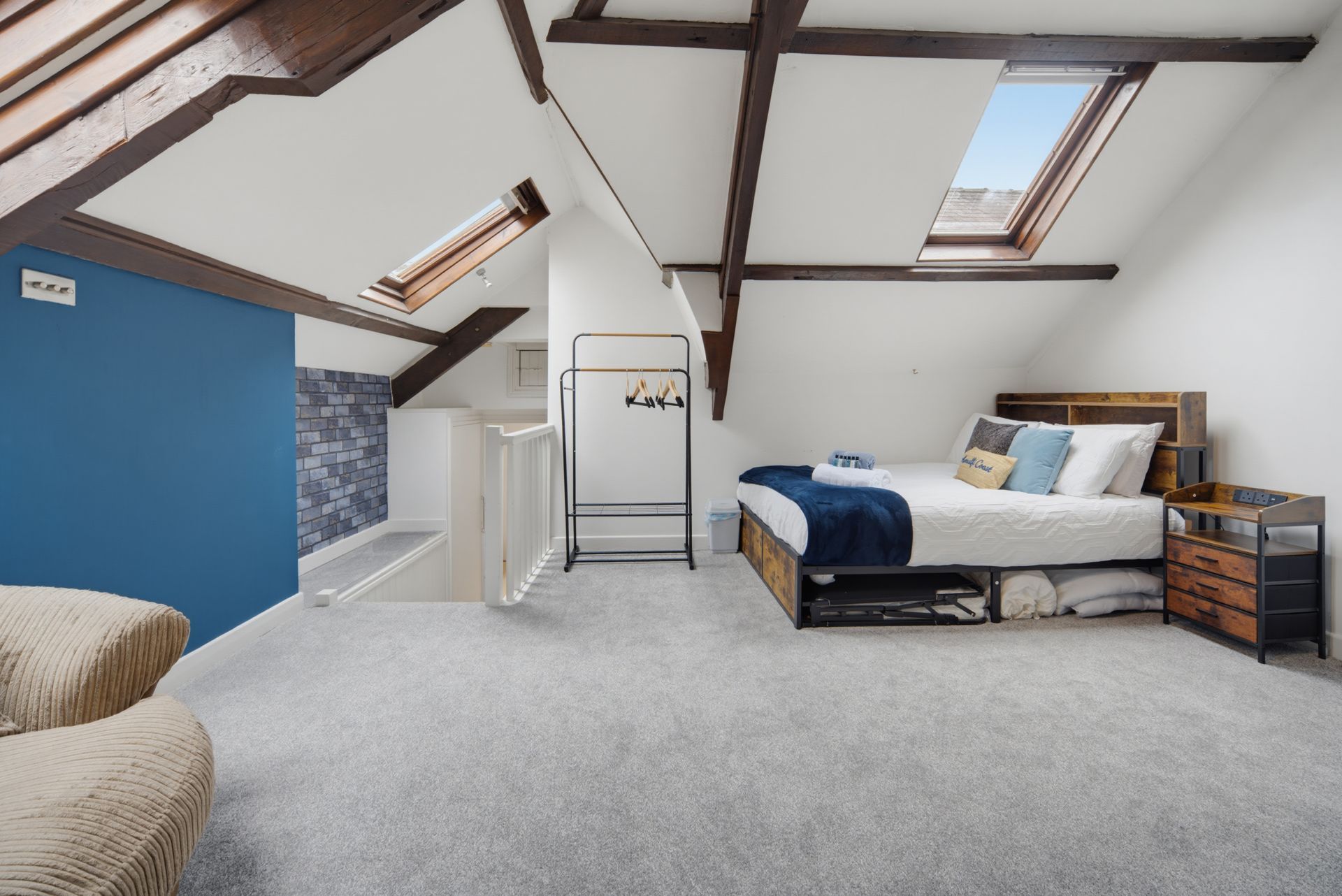 Bright attic bedroom with skylights, blue accent wall, and a bed beside a small dresser.