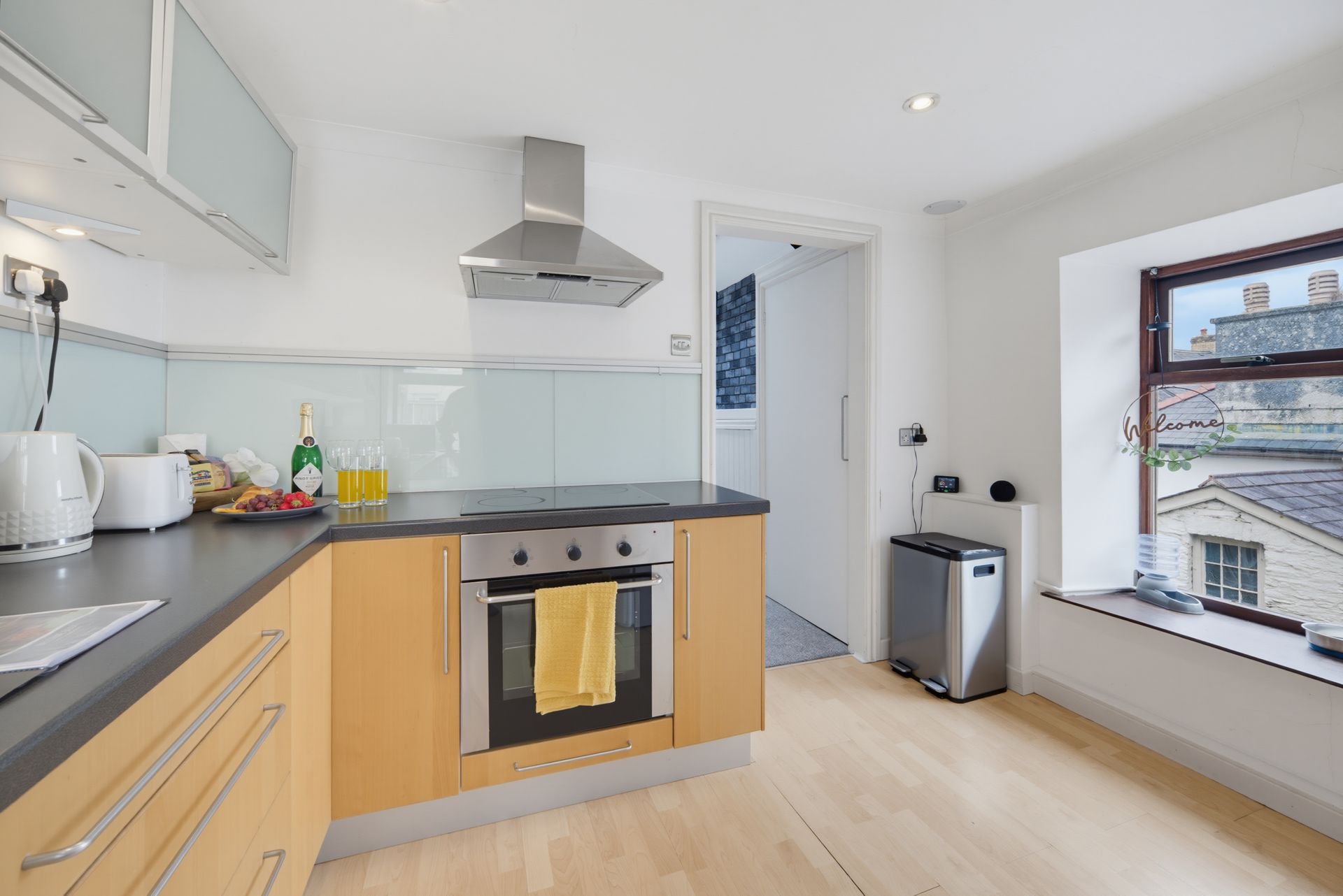 Modern kitchen with light wood cabinets, black countertops, stainless range hood, and a window seat by the window
