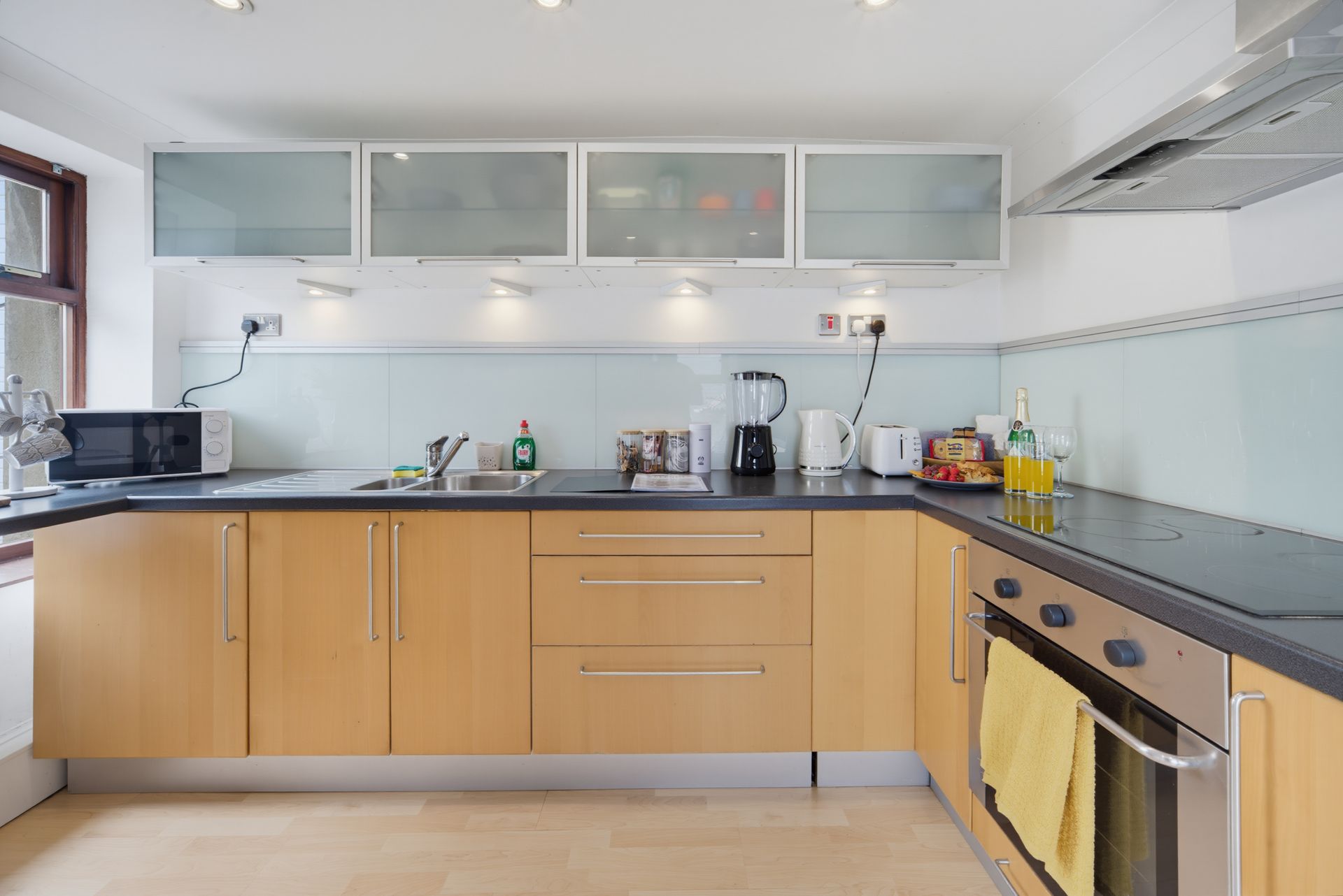 Modern kitchen with light wood cabinets, black countertops, and frosted glass wall cabinets