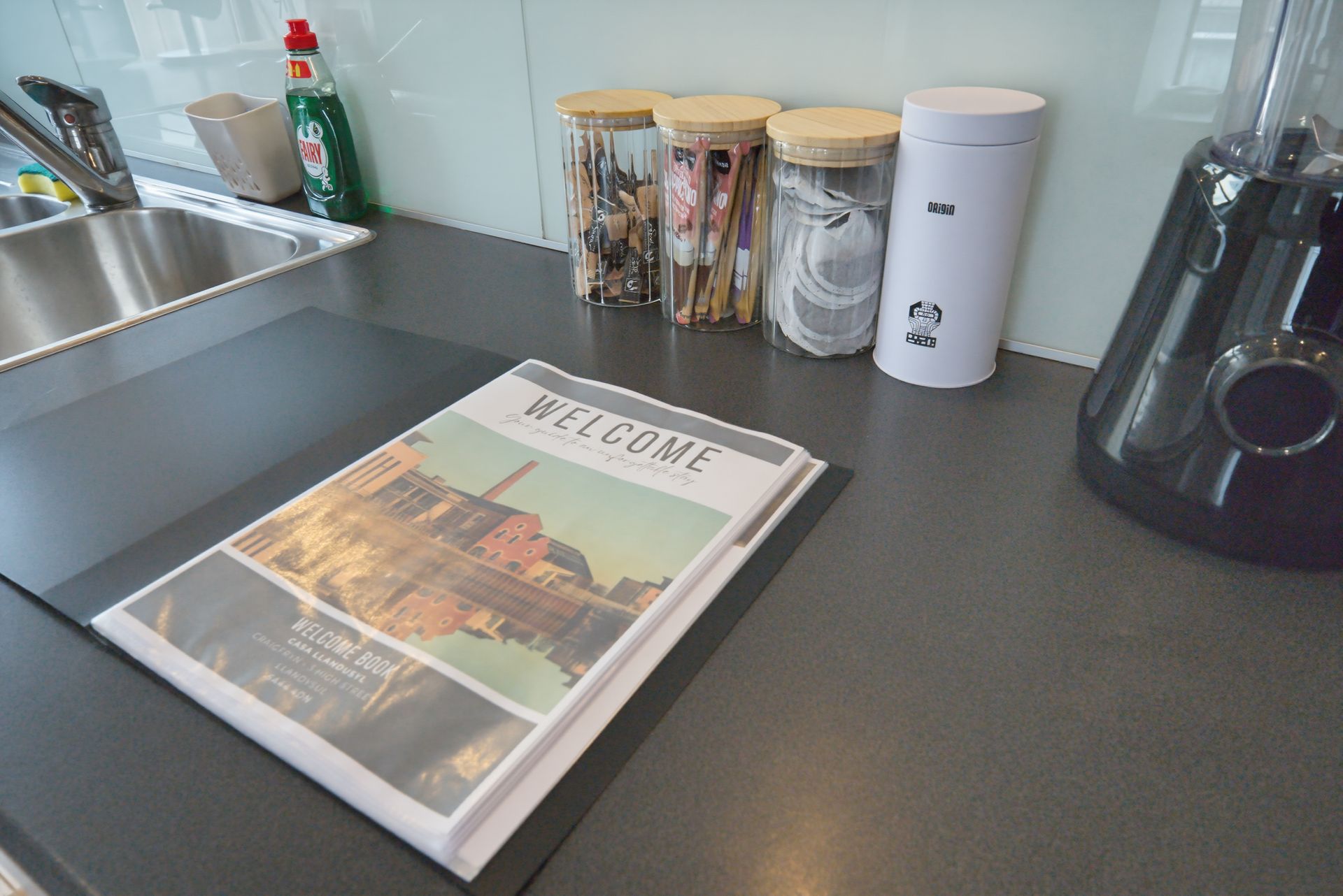 Kitchen counter with a cookbook, jars, sink, and small appliances.