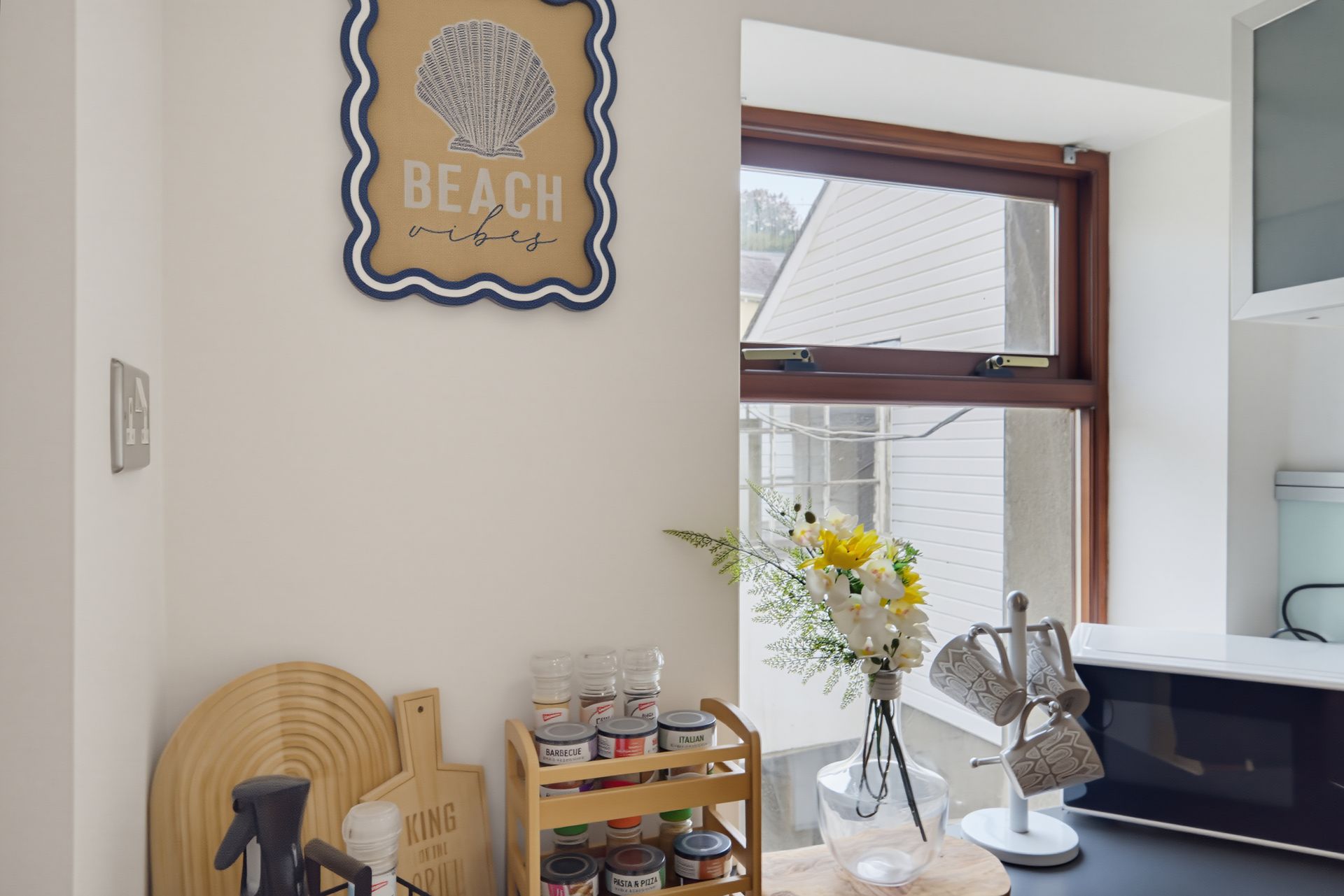 Beach-themed wall art above a small table with flowers, books, and a lamp by a window.