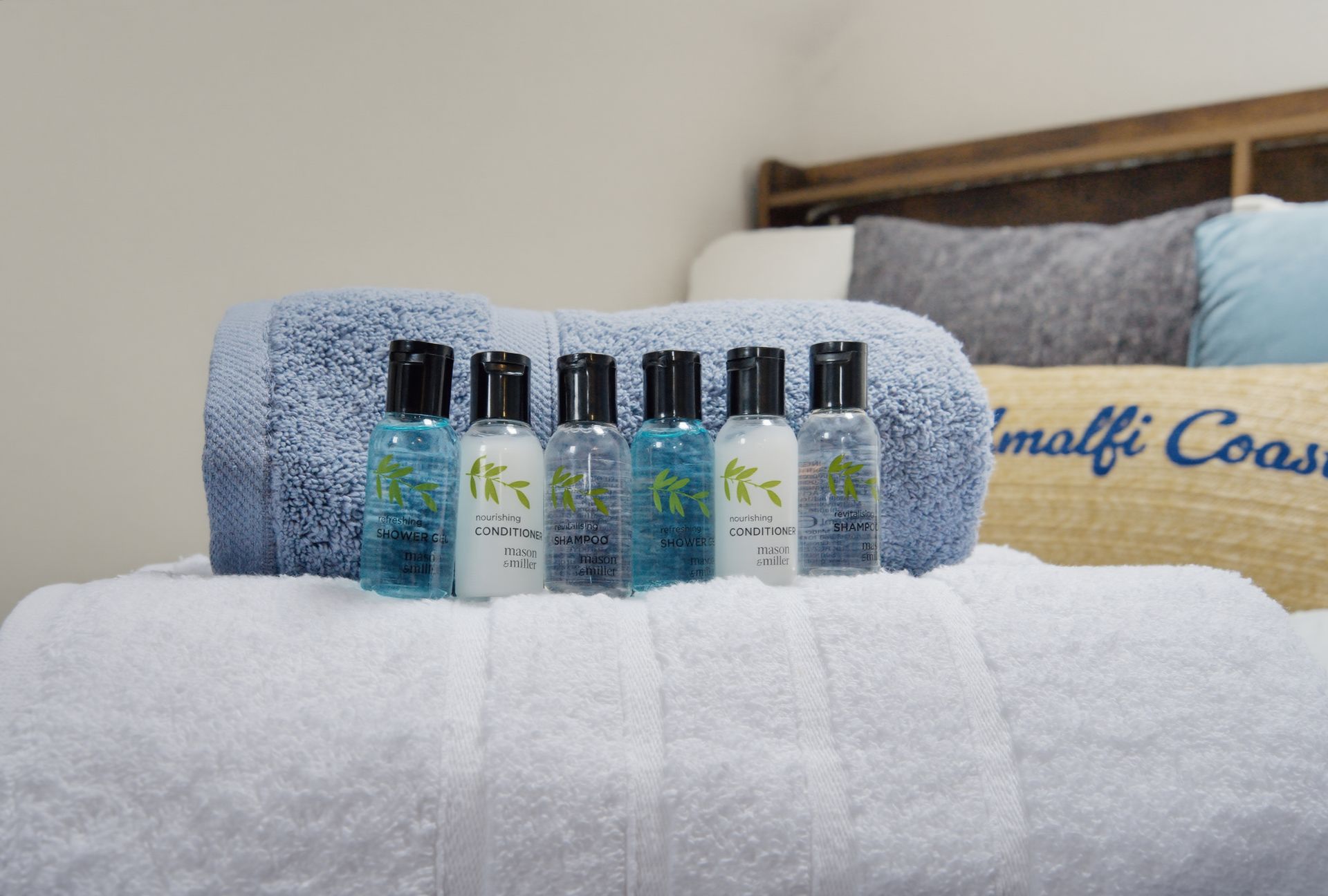 Six blue and white toiletry bottles lined up on a white towel in a bedroom.