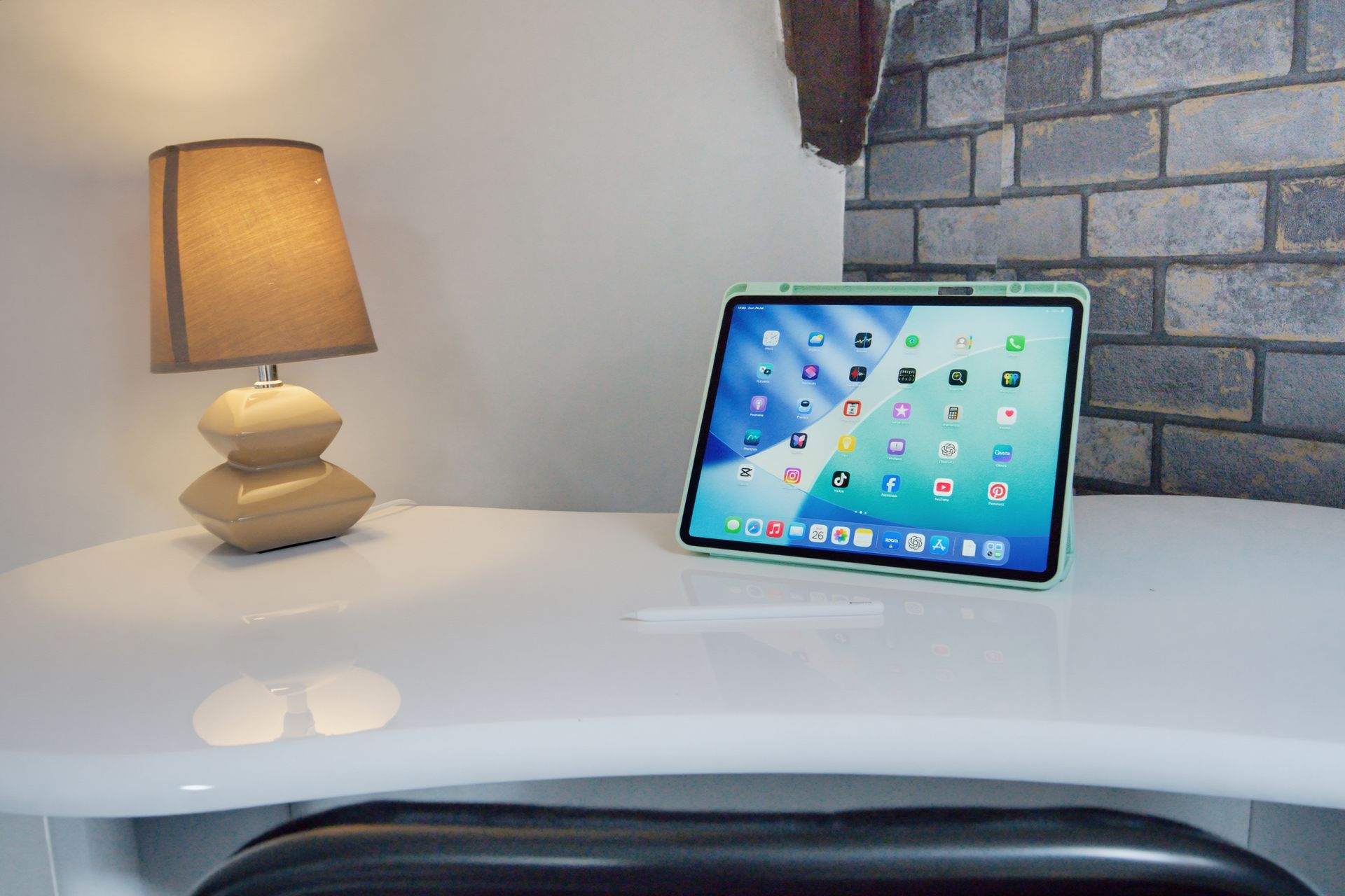Desk with lit lamp and a tablet on a white surface beside a brick wall