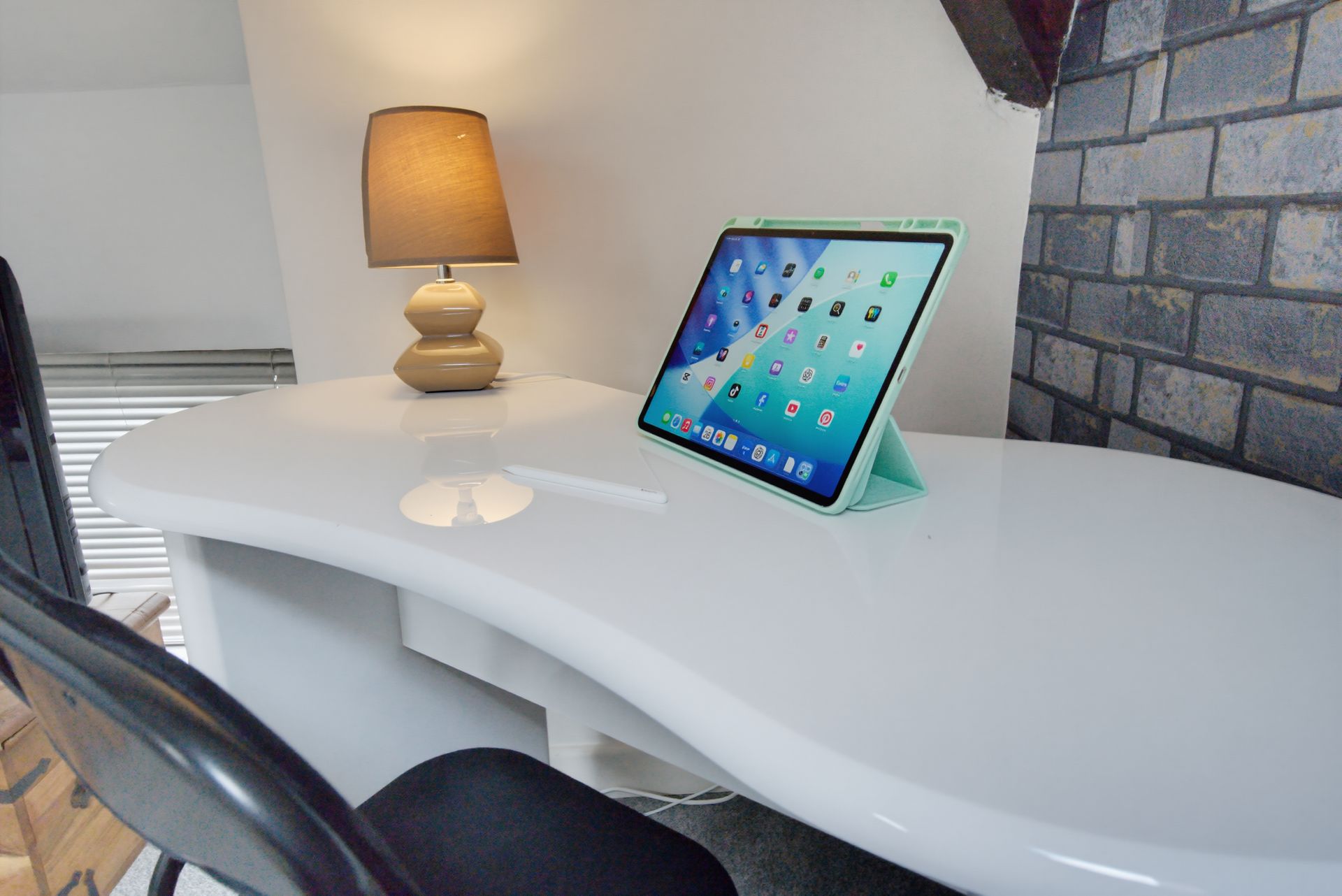 Modern desk with lit lamp and tablet on a white surface in a brick-walled room