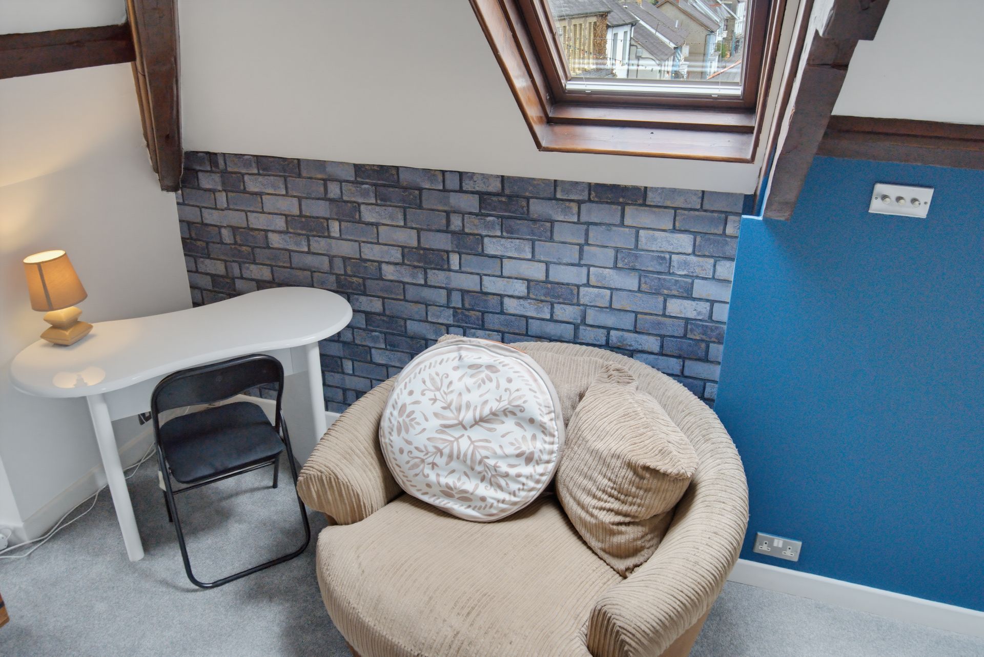 Small attic nook with desk, chair, beige armchair, skylight, stone accent wall, and blue wall.