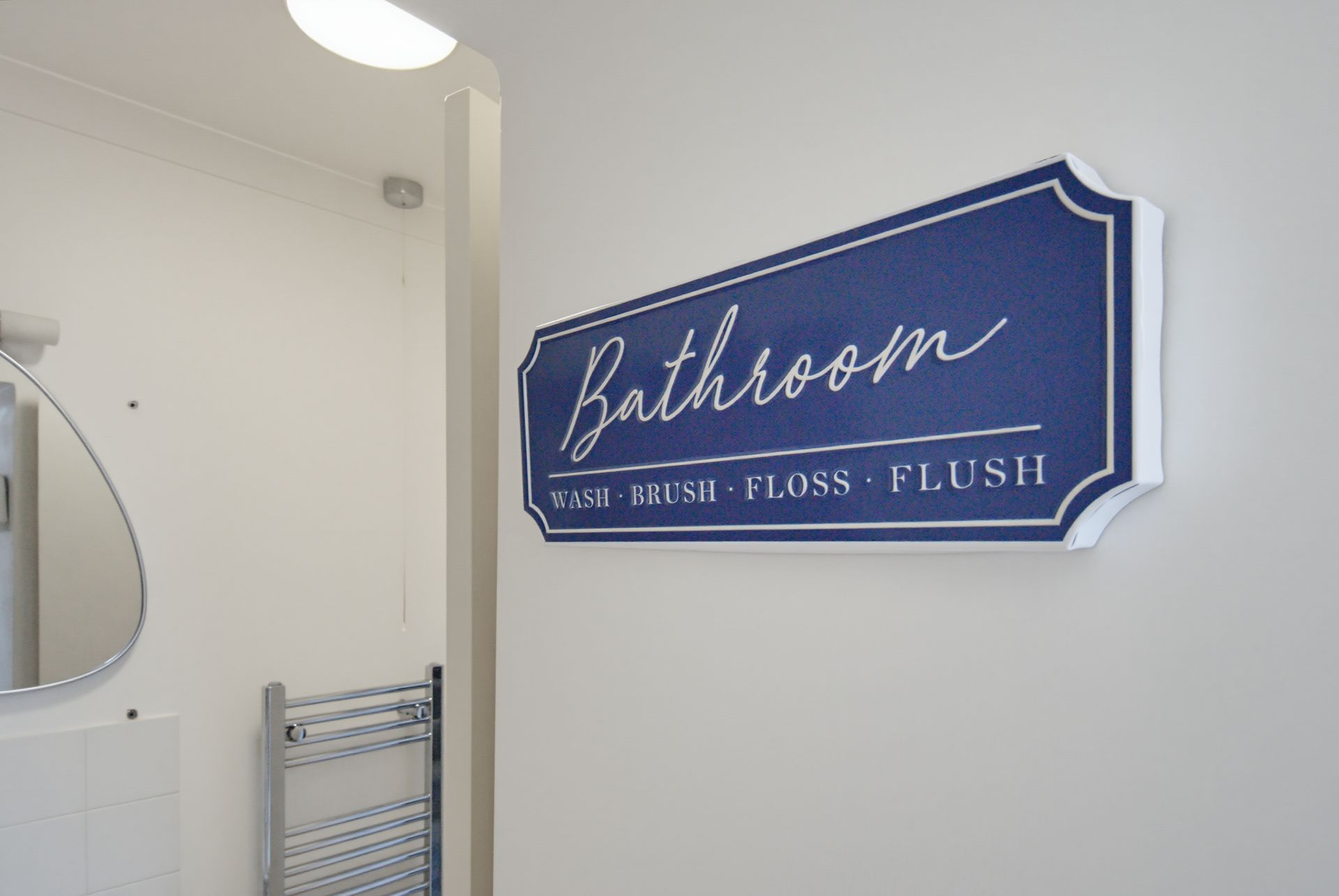 Blue bathroom sign reading “flush flush flush” on a white wall in a restroom.
