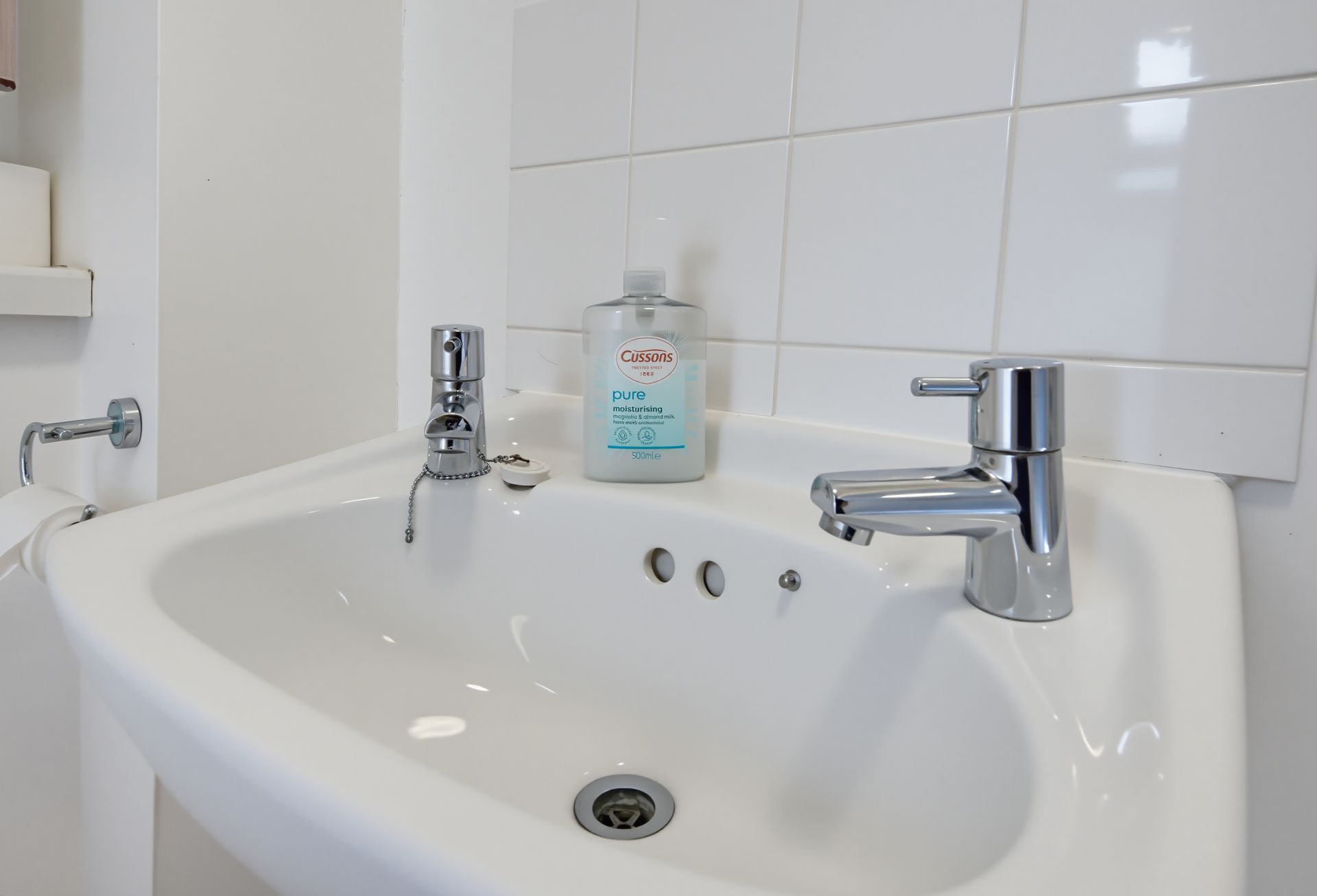 White bathroom sink with chrome faucet and soap dispenser against tiled wall