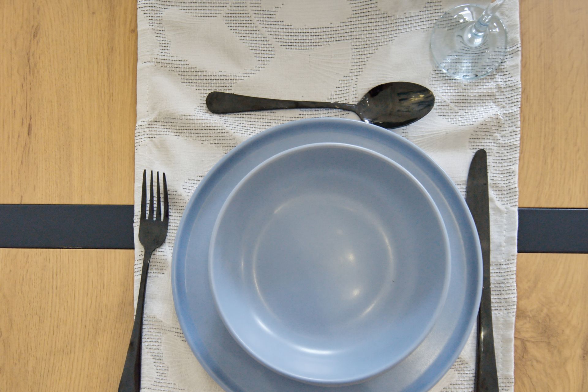 Blue bowl with utensils and a water glass set on a table placemat