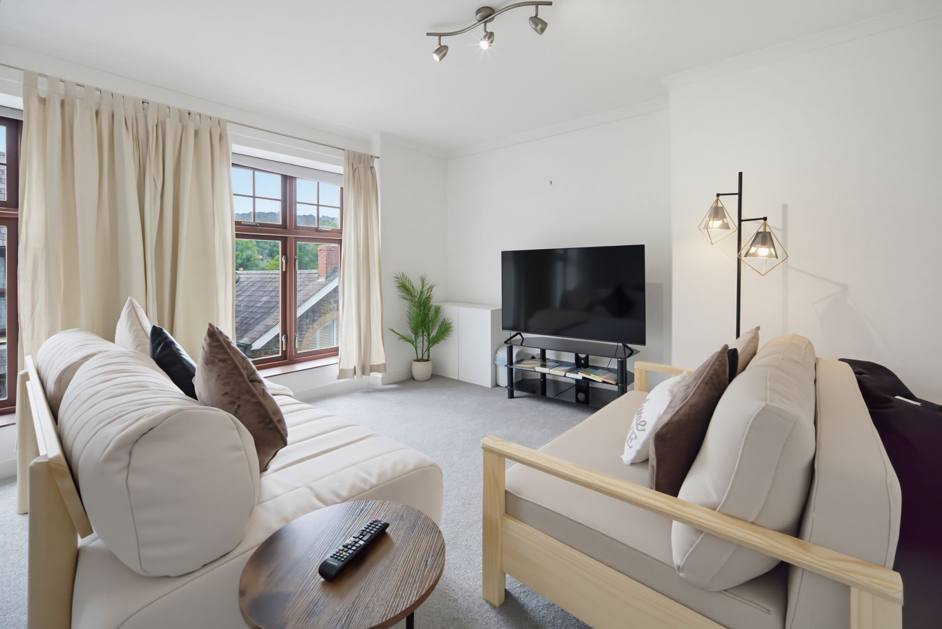 Bright living room with cream sofas, TV, coffee table, and large window with curtains