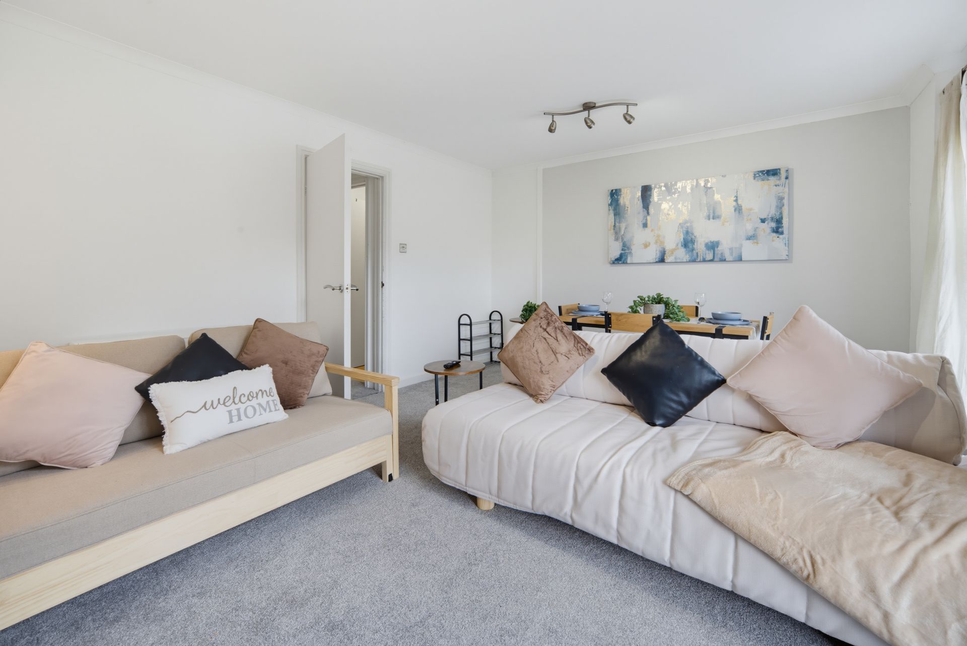 Bright modern living room with two beige sofas, decorative pillows, and abstract wall art