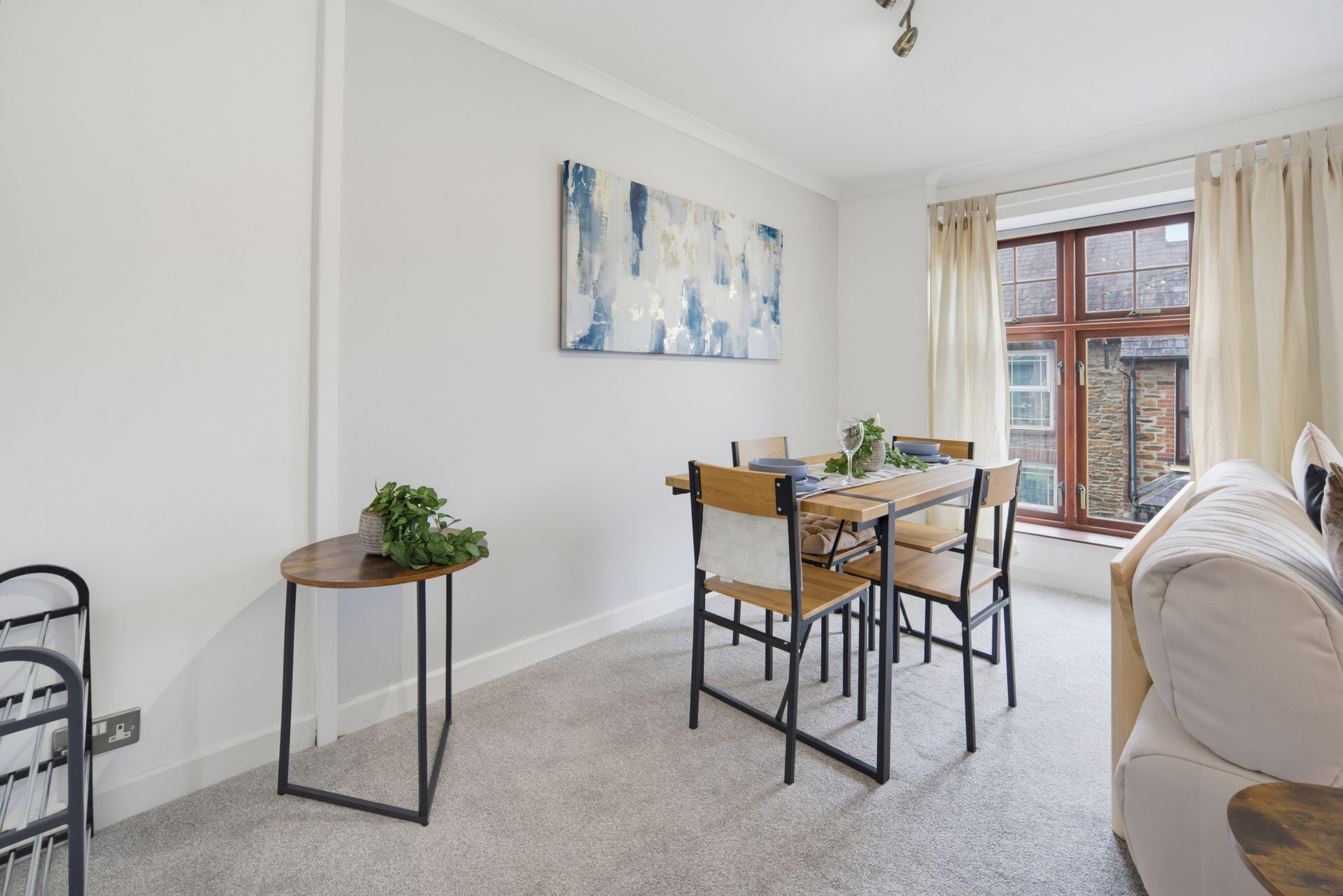 Bright dining area with a wooden table, black chairs, wall art, and large window beside a sofa