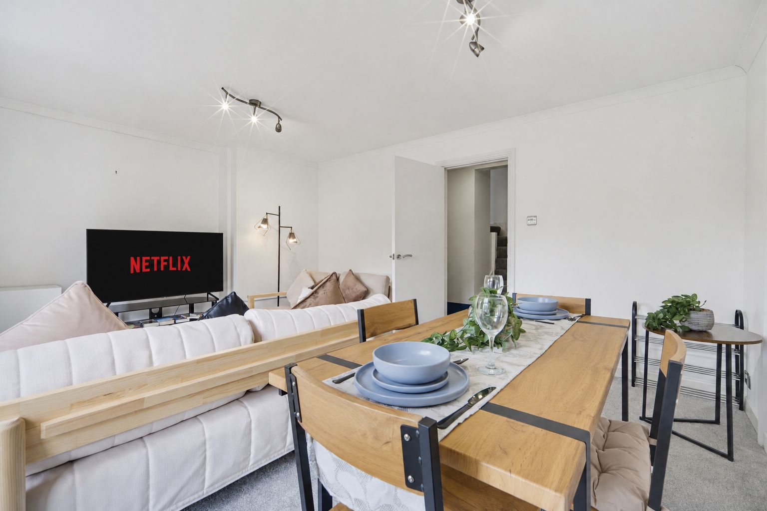 Bright living room with white sofas, dining table, and TV showing Netflix.