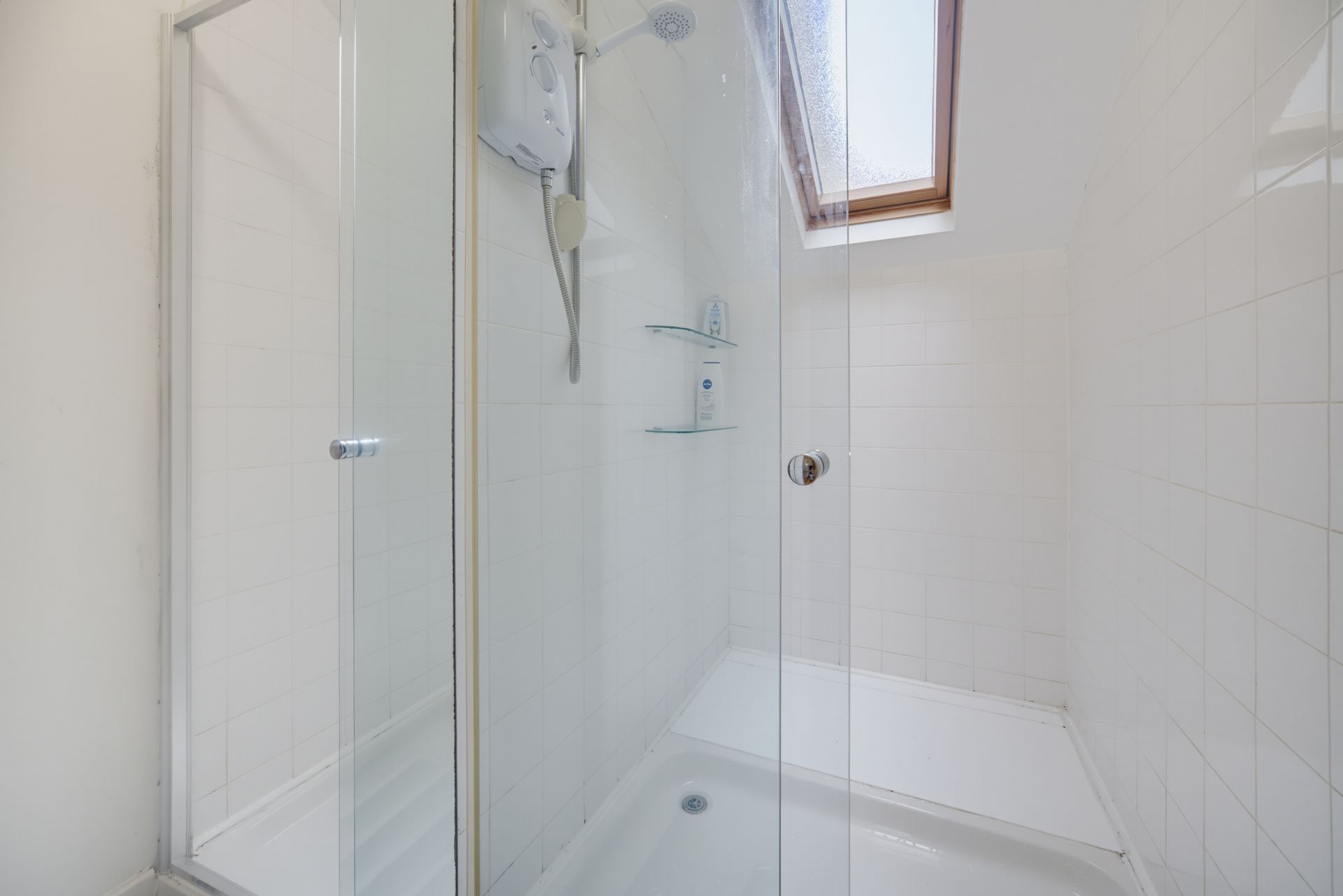 Small white tiled bathroom with a glass shower enclosure and a skylight above the tub.