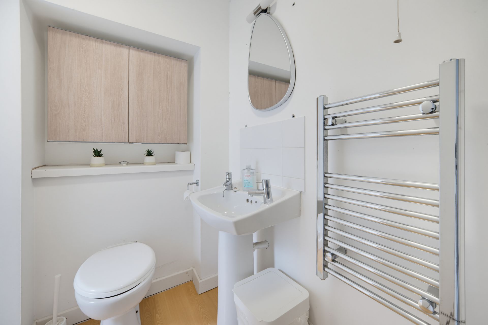 Bright white bathroom with toilet, sink, mirror, towel radiator, and a frosted window ledge